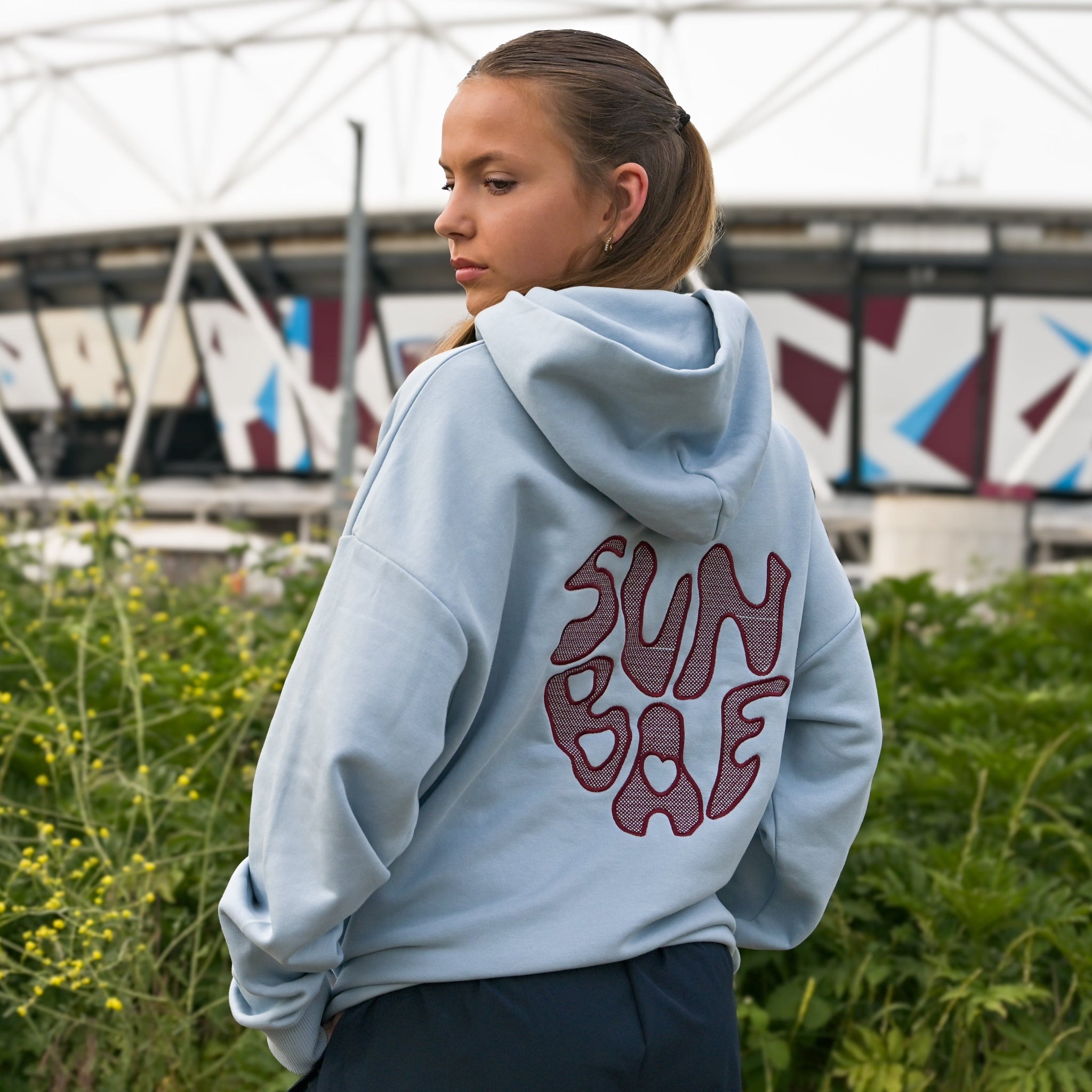 Yvonne Main wearing a hoodie with 'Sunbae' text in front of a stadium.
