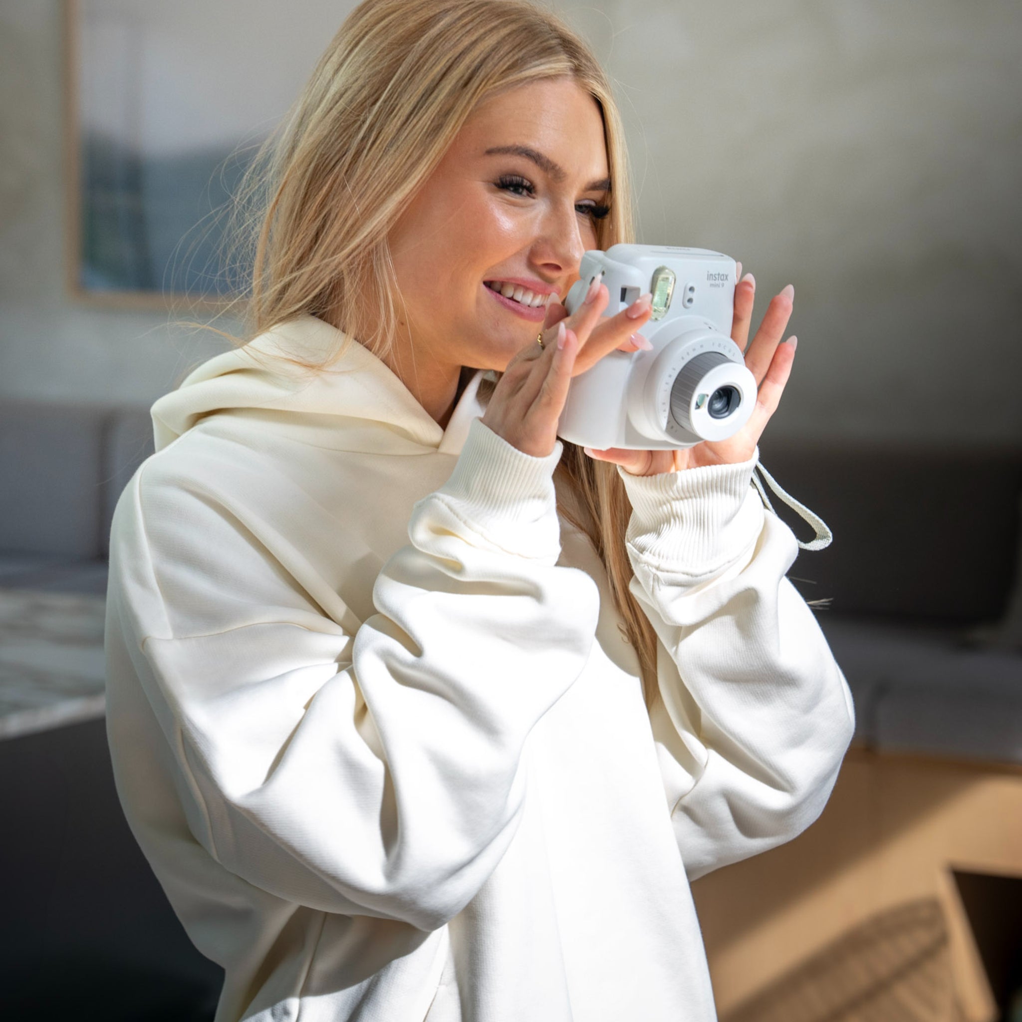 A person wearing a white oversized Sunbae hoodie with a logo, holding a white camera and taking a photo.