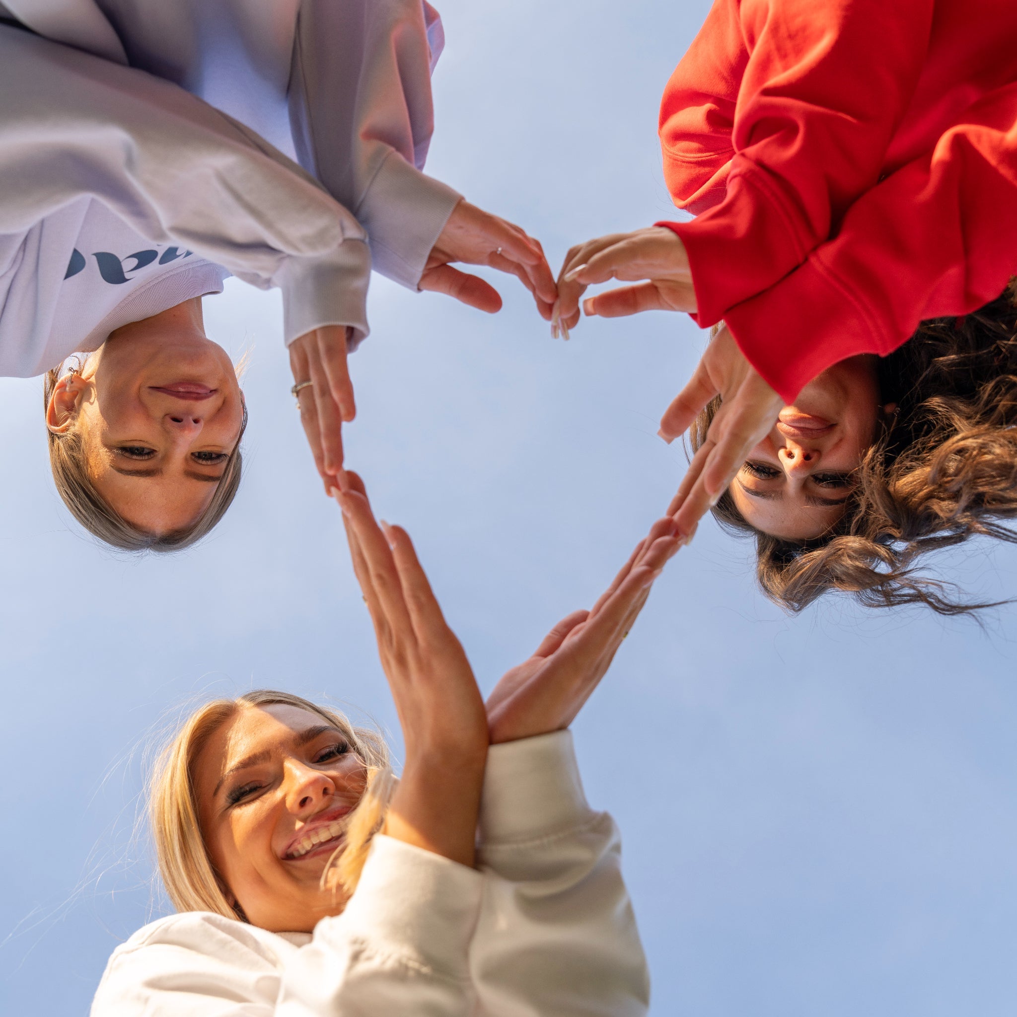Sunbae Glow Collective making a heart with their hands against a clear blue sky.
