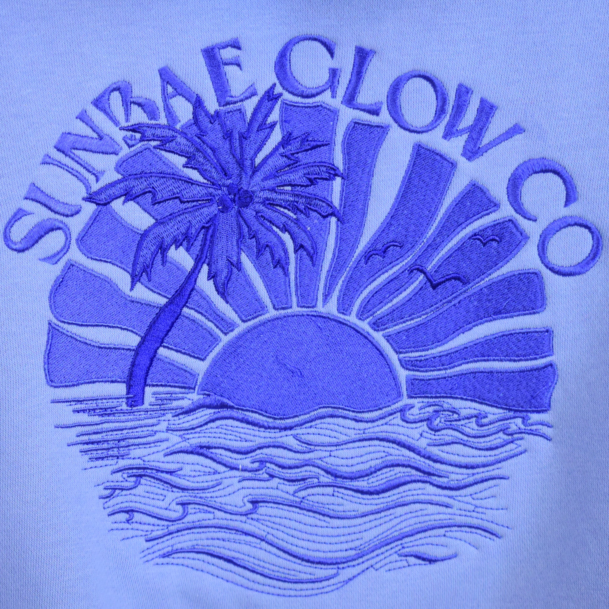Blue SUNBAE Tidal Glow logo with palm tree, sun, and waves on a light blue background