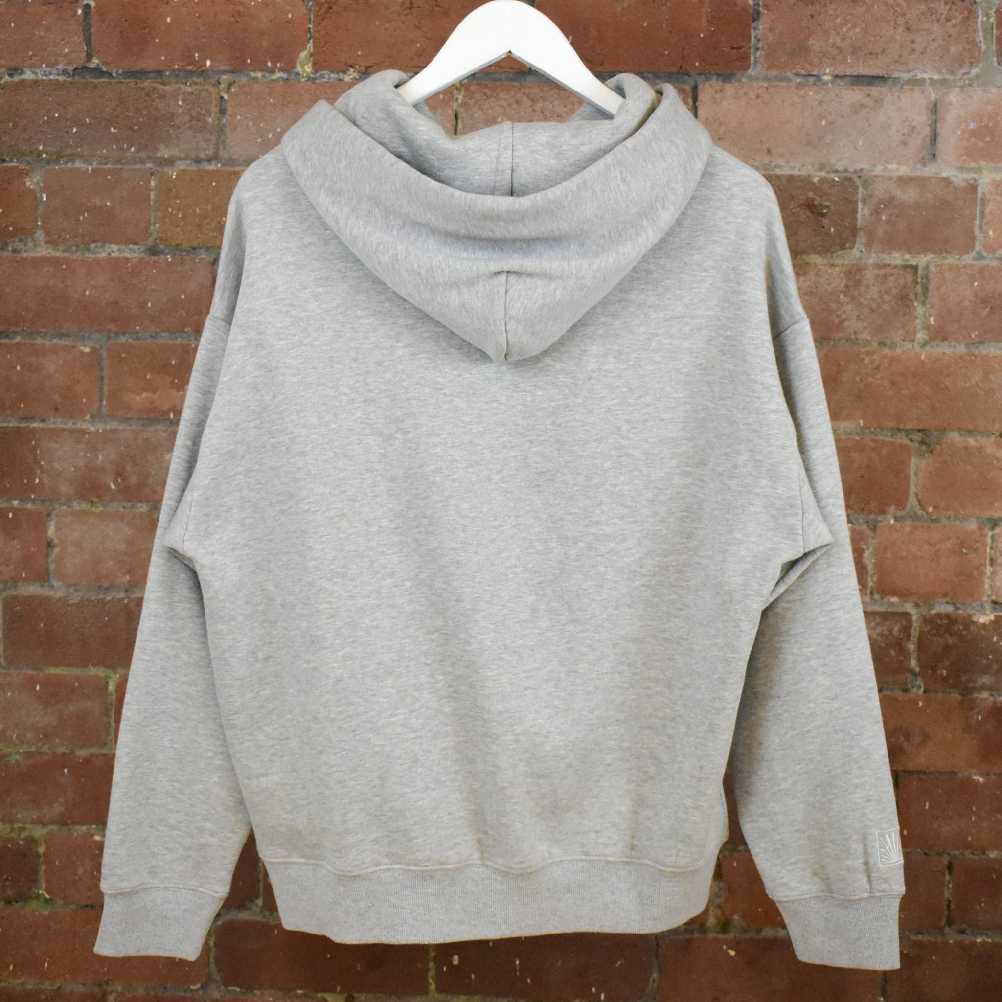 Grey Sunbae hoodie on a hanger against a brick wall