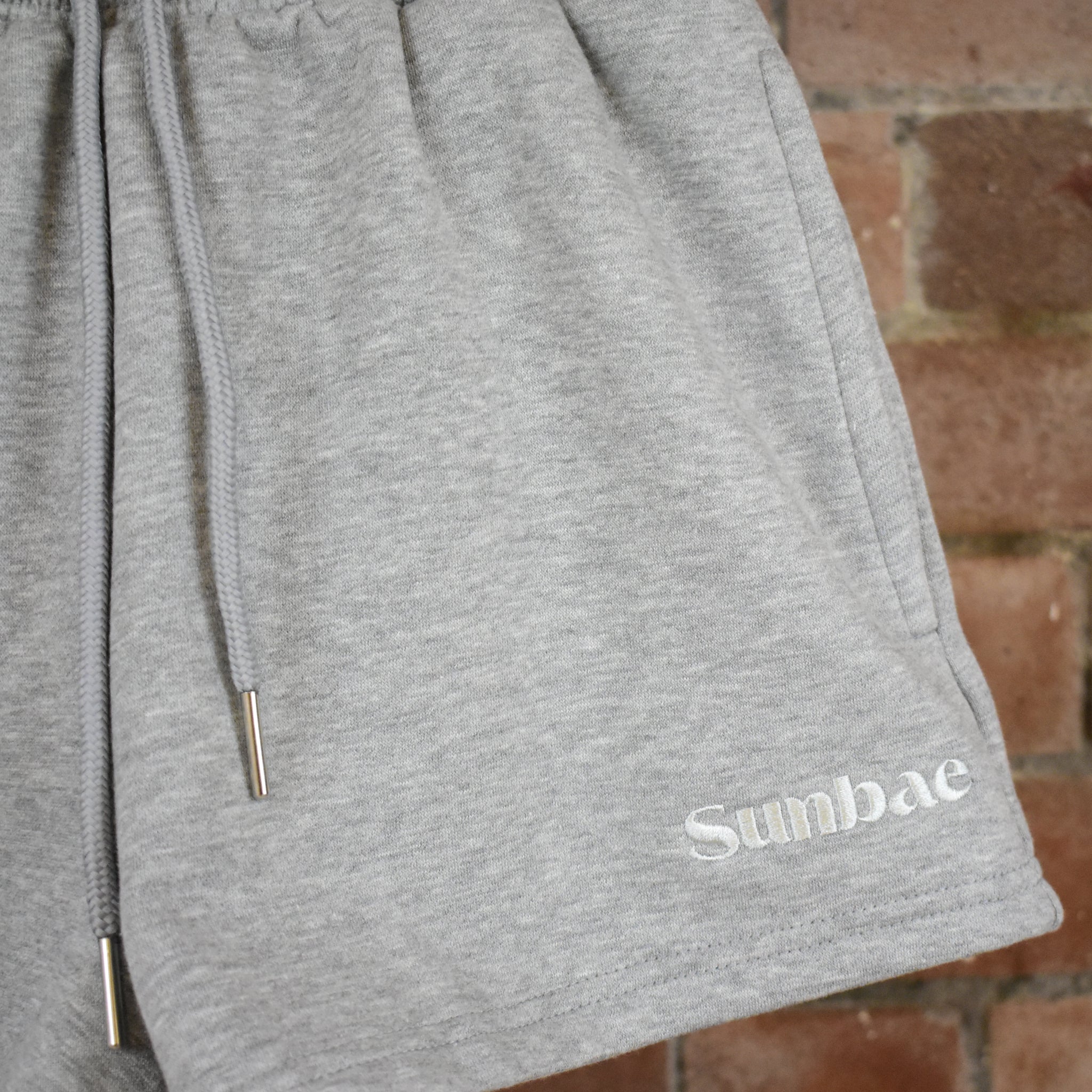 Grey sweat short with SUNBAE branding on a brick wall background