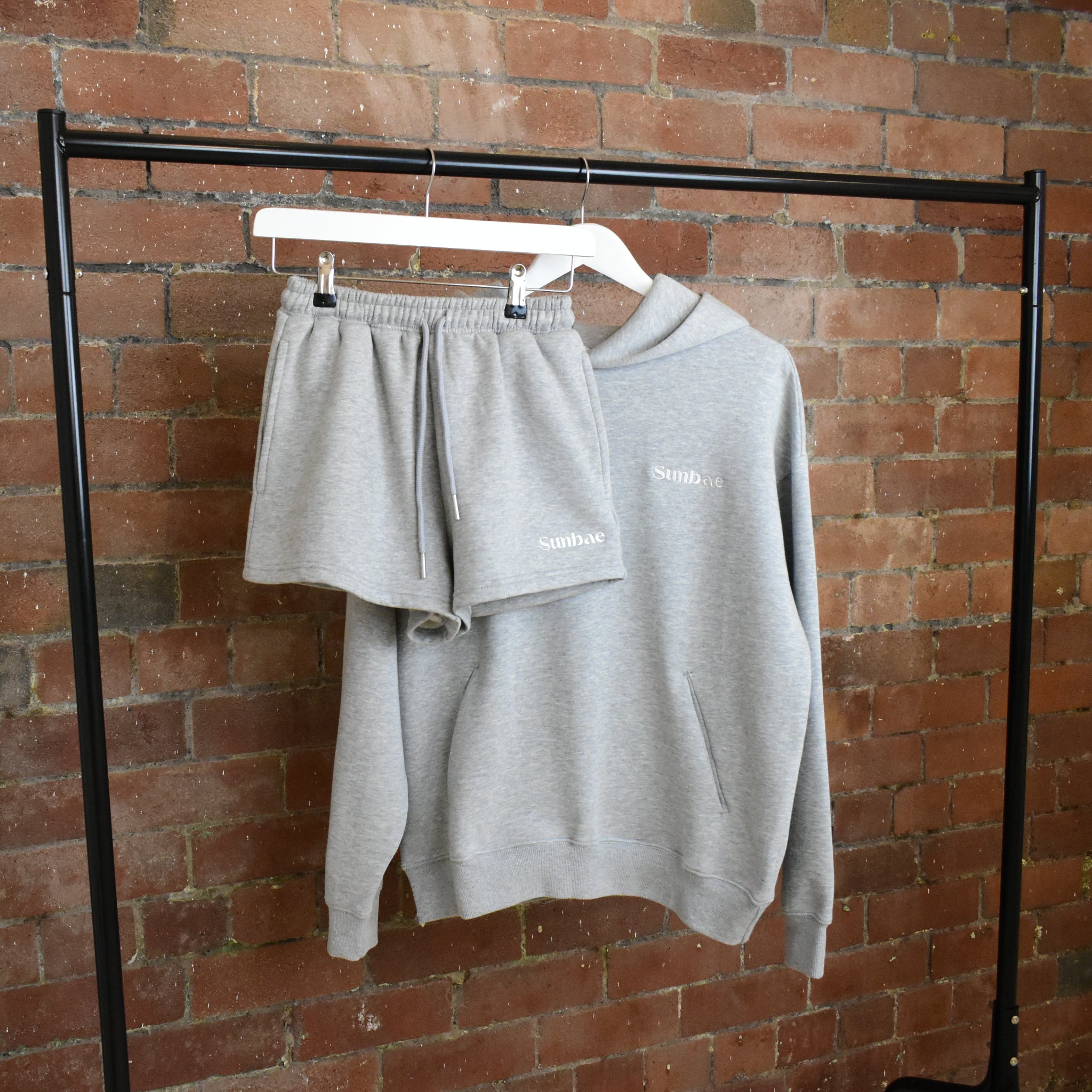 SUNBAE Grey sweatshirt and shorts set on a hanger against a brick wall.