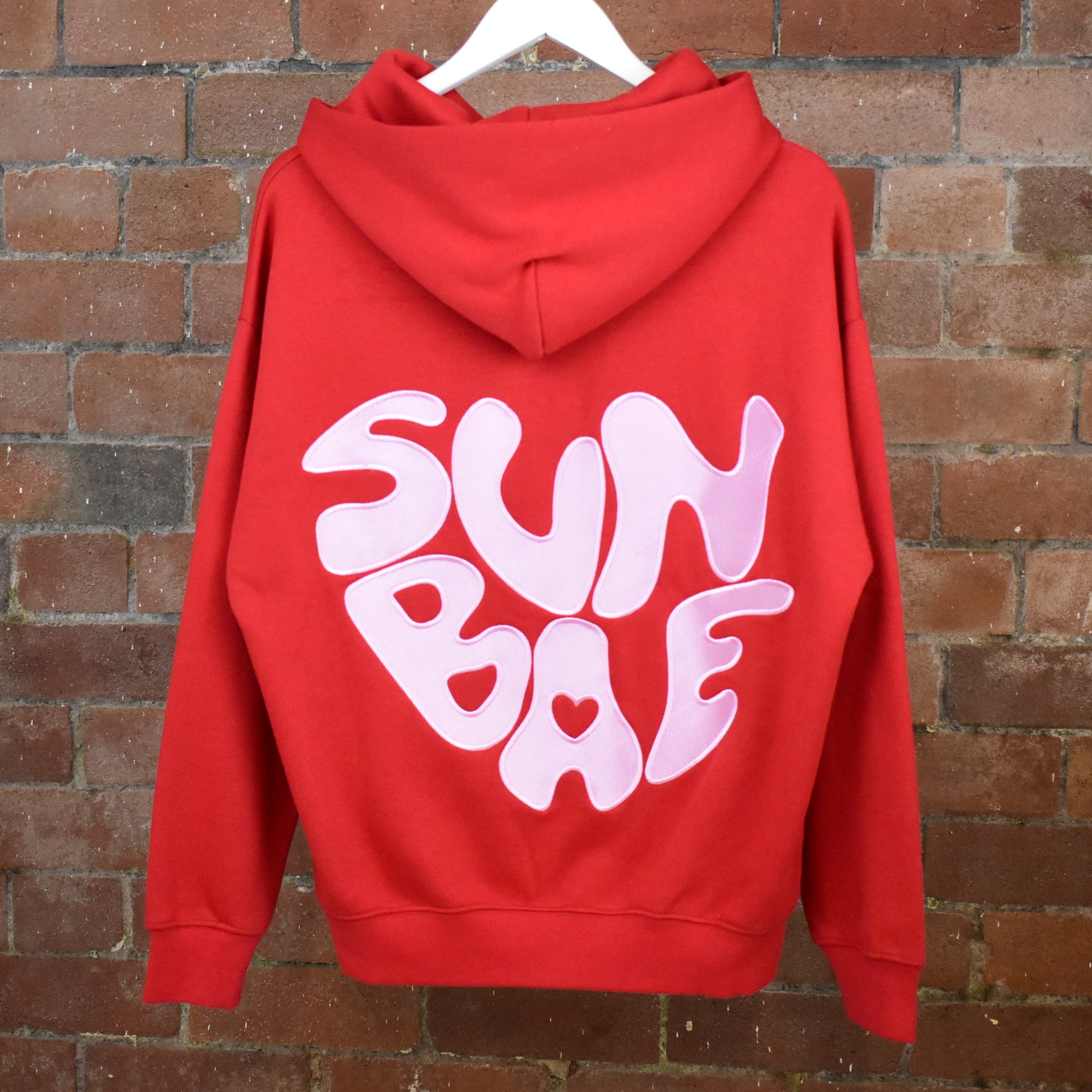 Reverse of Red SUNBAE hoodie on a brick wall background