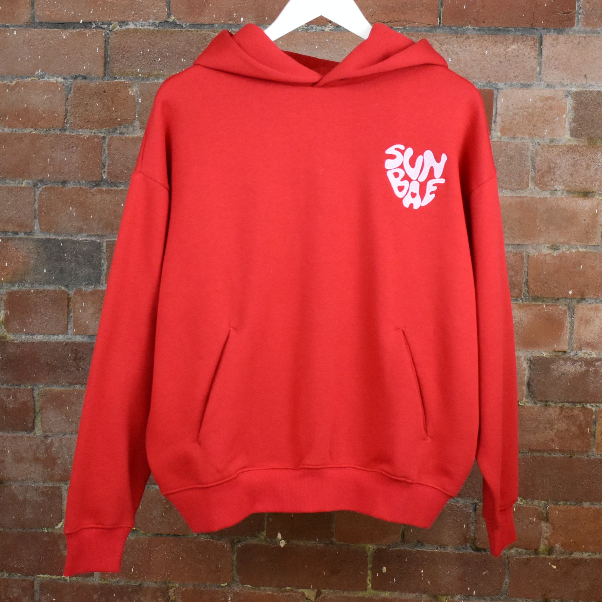 Red SUNBAE hoodie on a brick wall background
