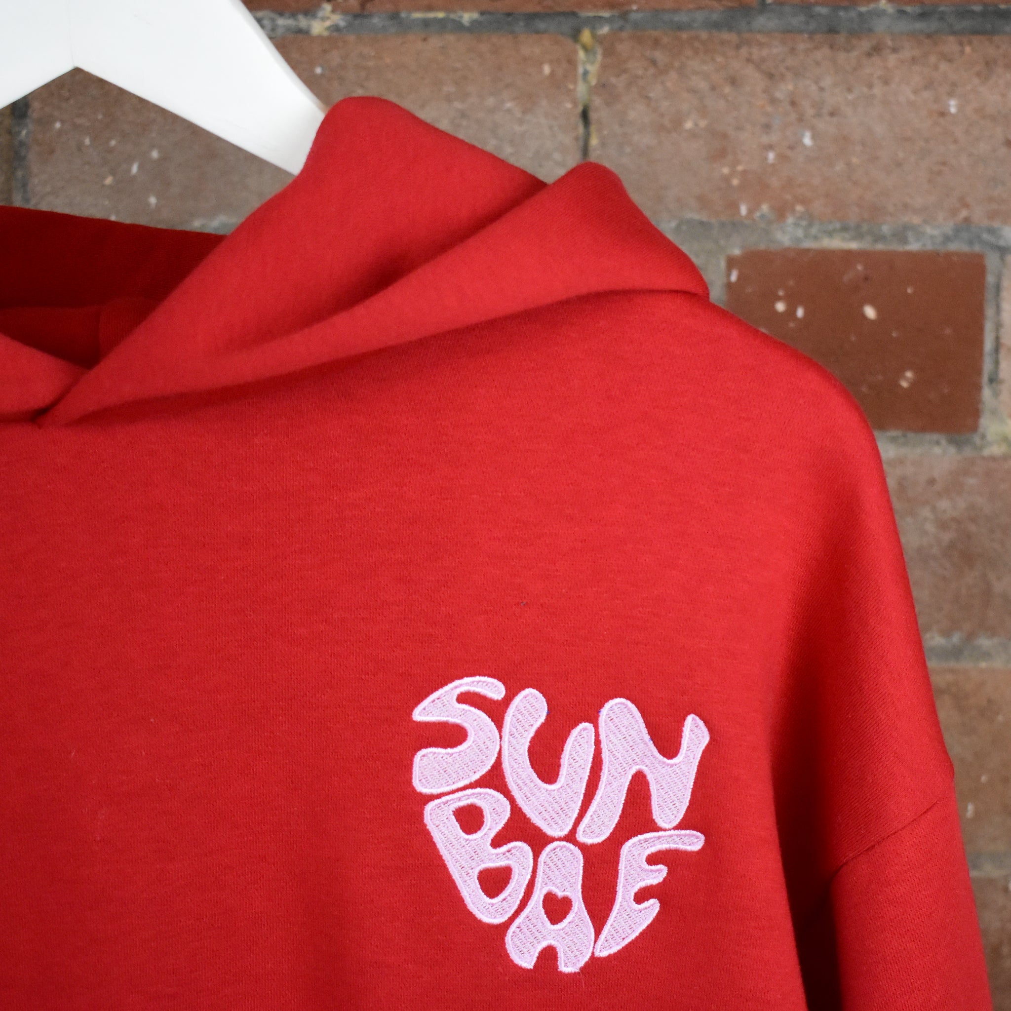 Red SUNBAE hoodie on a brick background