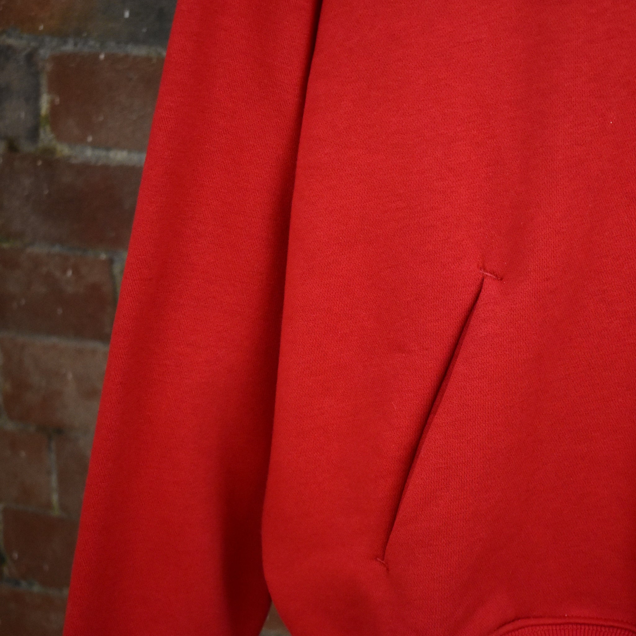 Close-up of a red SUNBAE Hoodie against a brick wall.