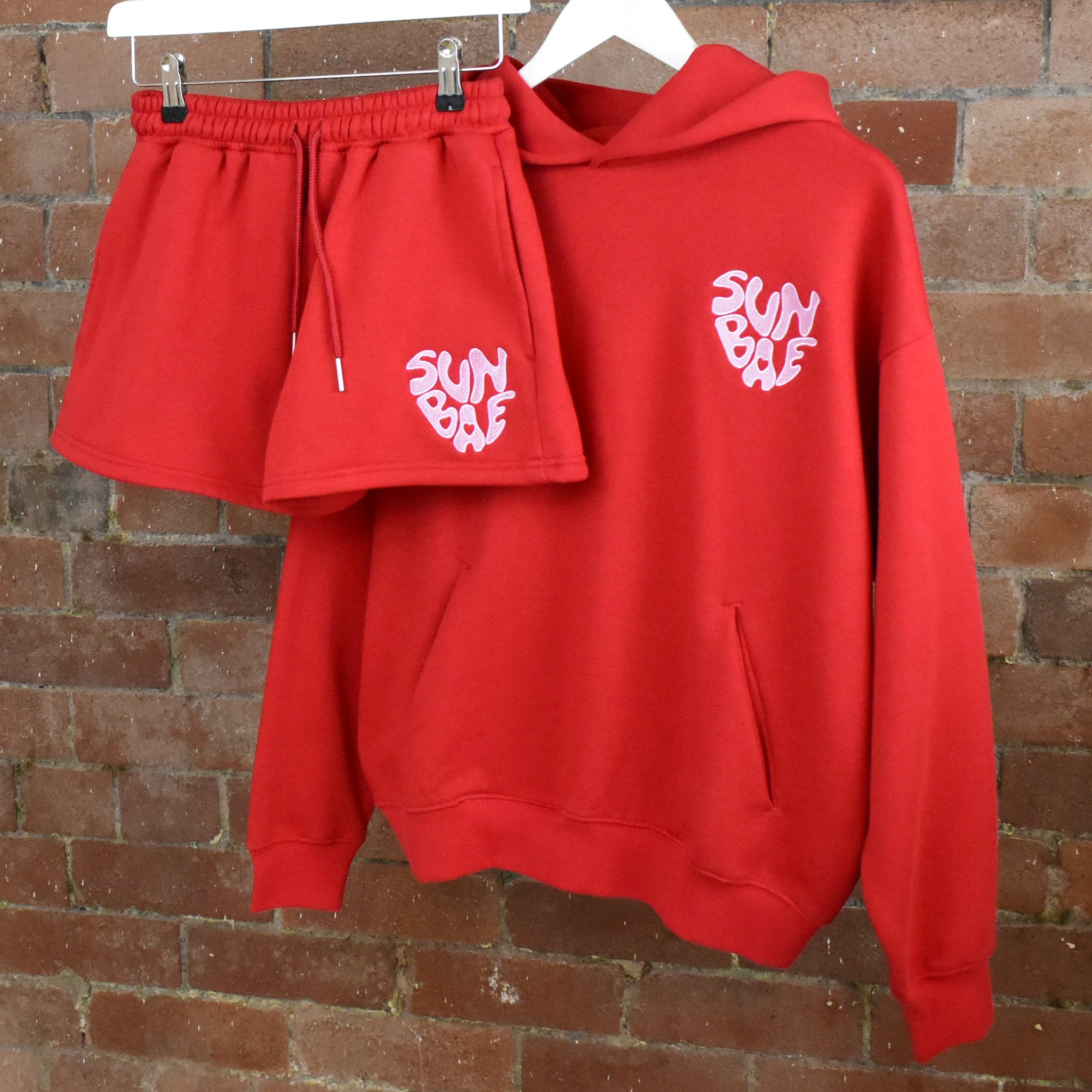 Red SUNBAE hoodie and shorts set on a brick wall background