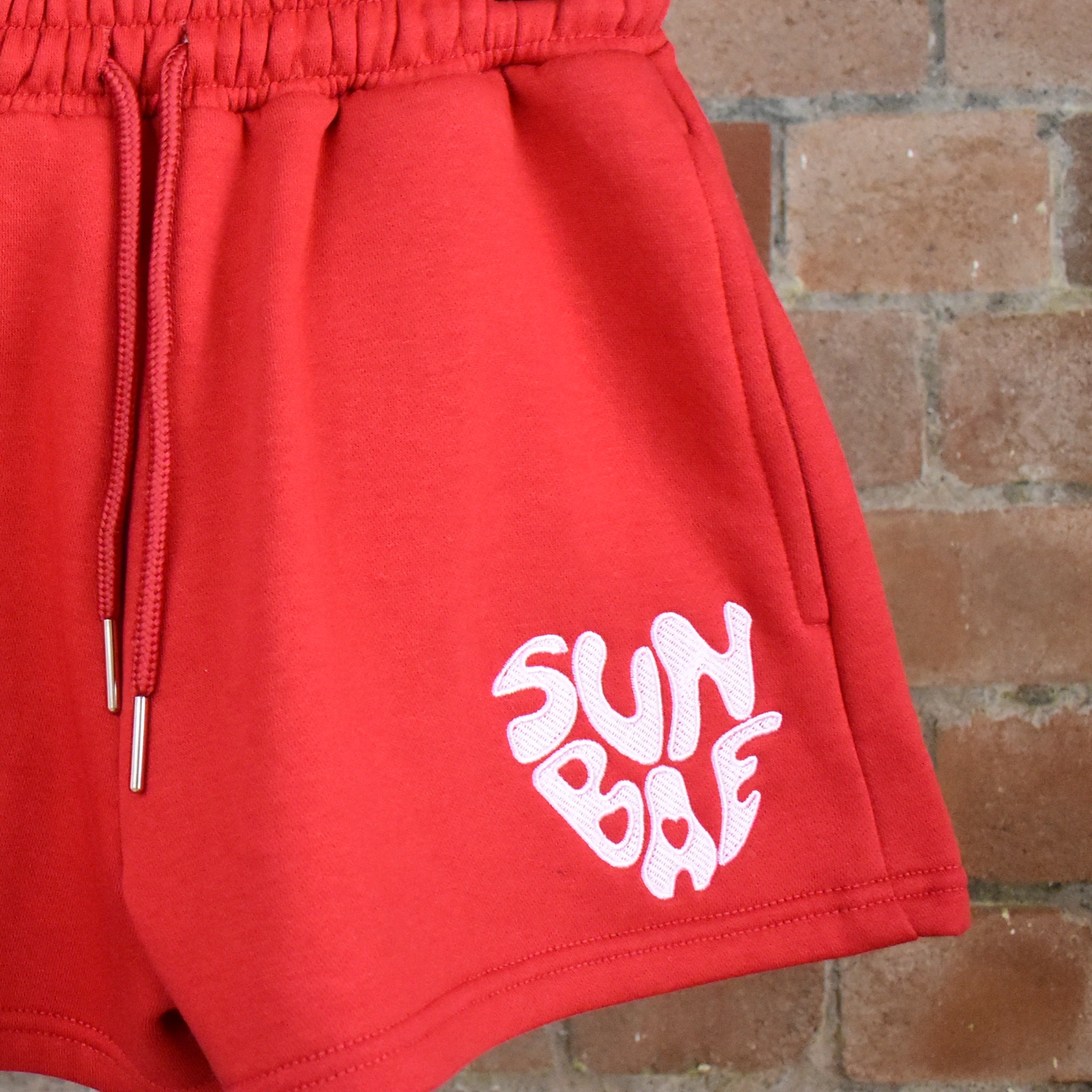 Red SUNBAE shorts on a brick wall background