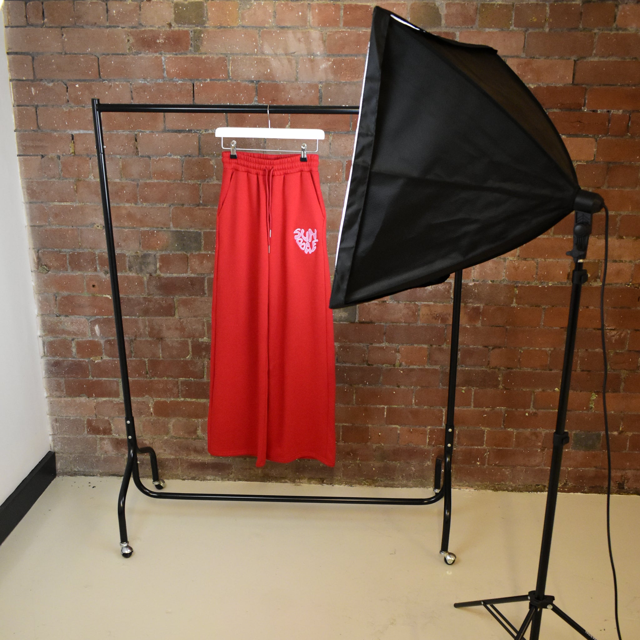 Red SUNBAE Sweat Pant skirt on a rack in front of a brick wall.