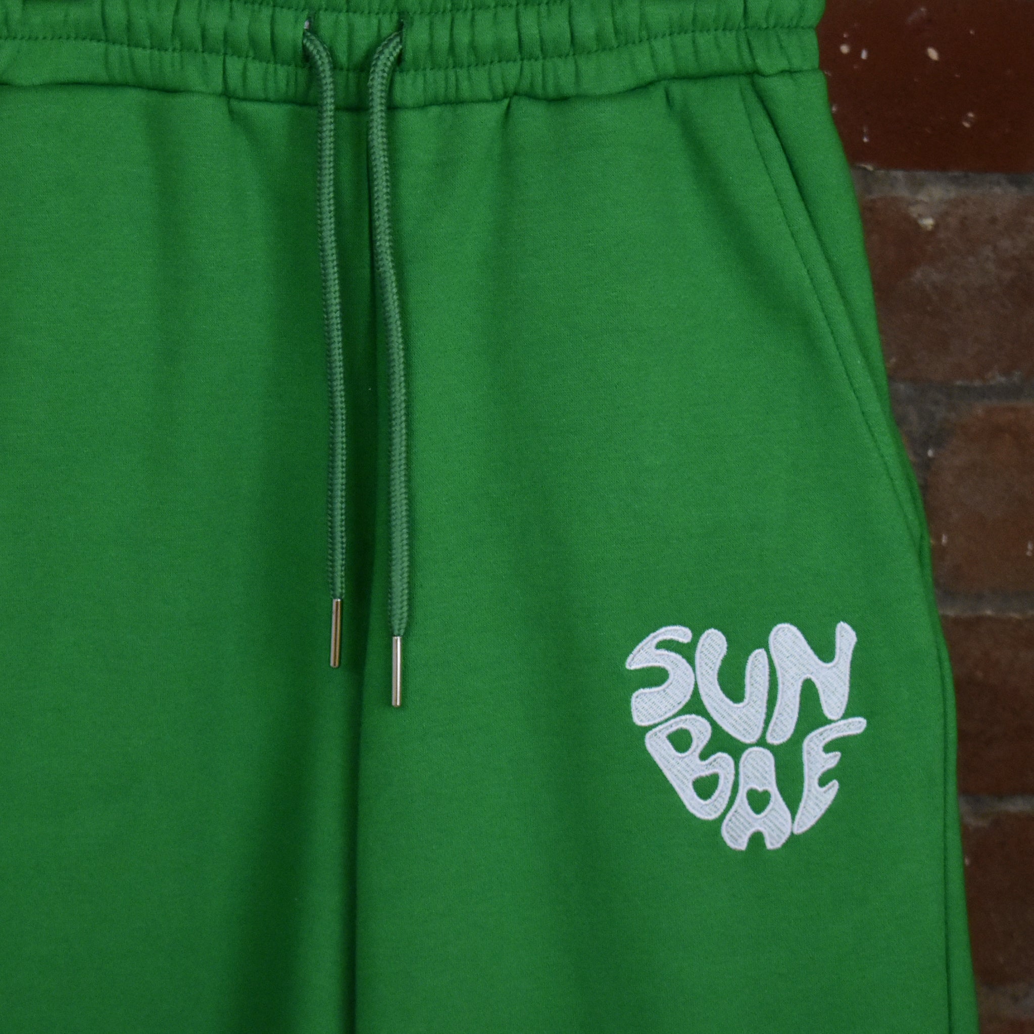 Green SUNBAE Sweat Pants on a brick wall background