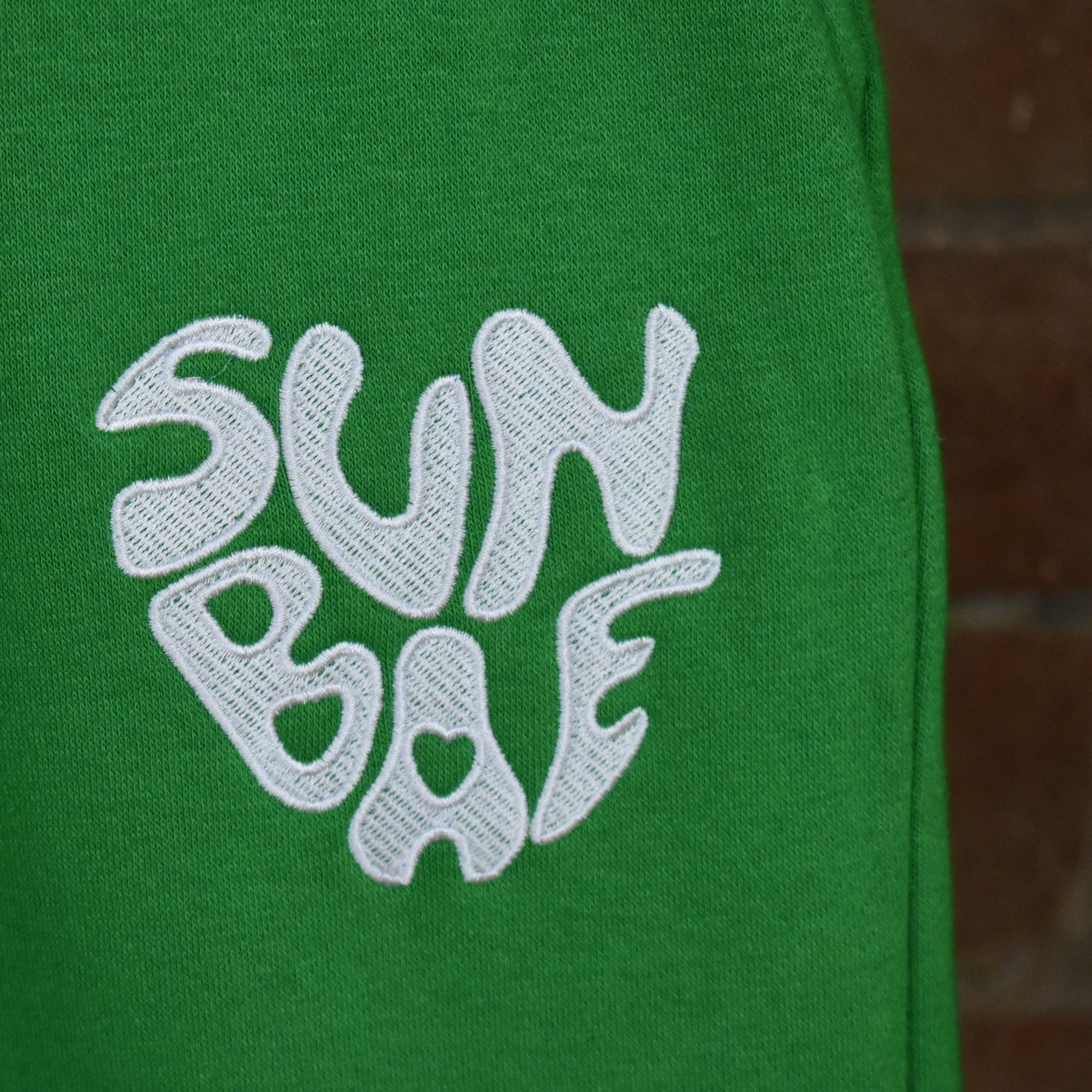 Green Sweat Pant with SUNBAE logo embroidered in white on a brick background