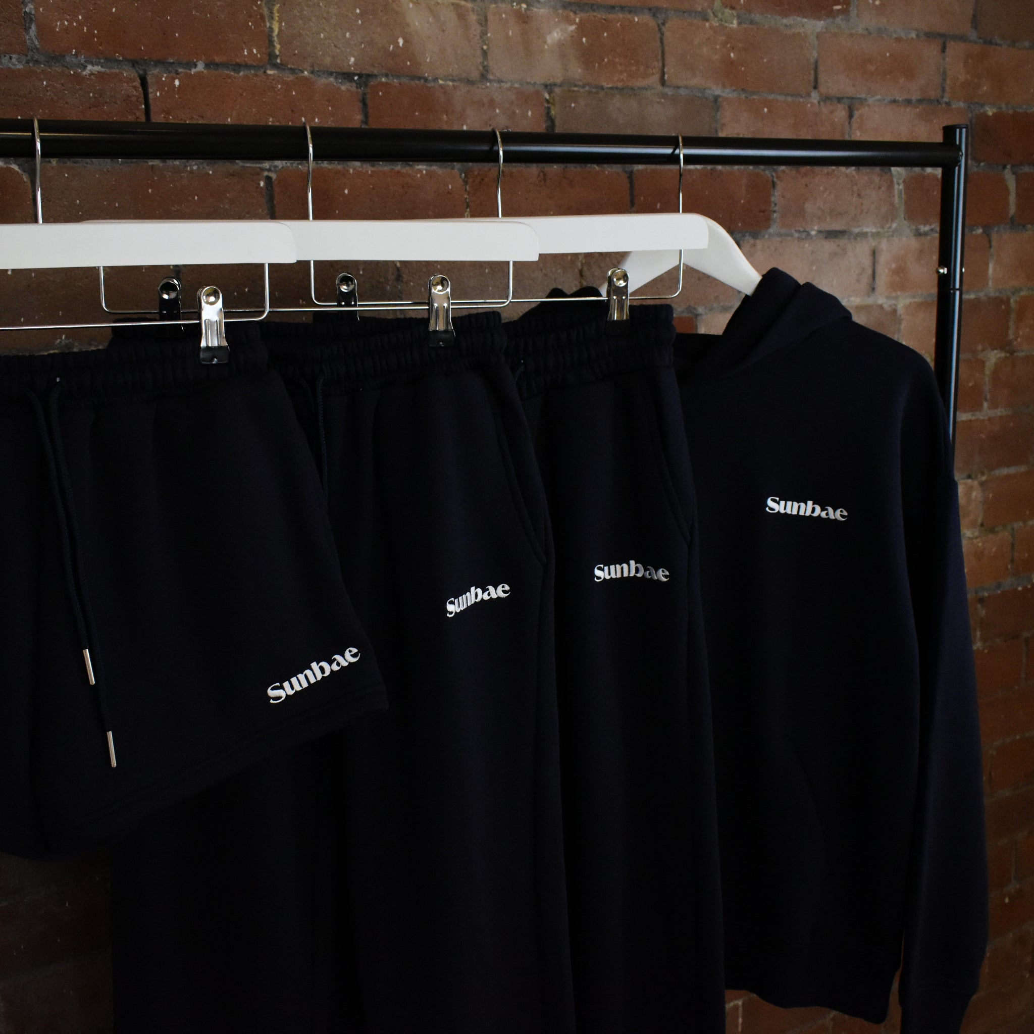 Navy SUNBAE collection on a rack against a brick wall.