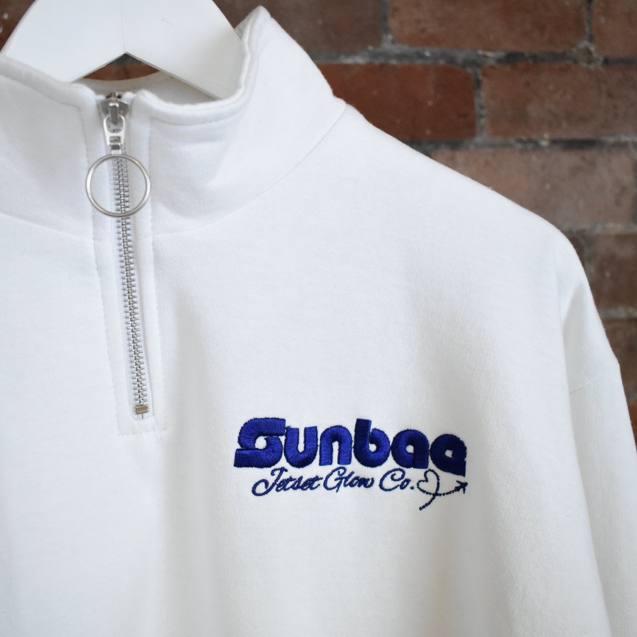 White SUNBAE half-zip sweatshirt with logo on a brick wall background
