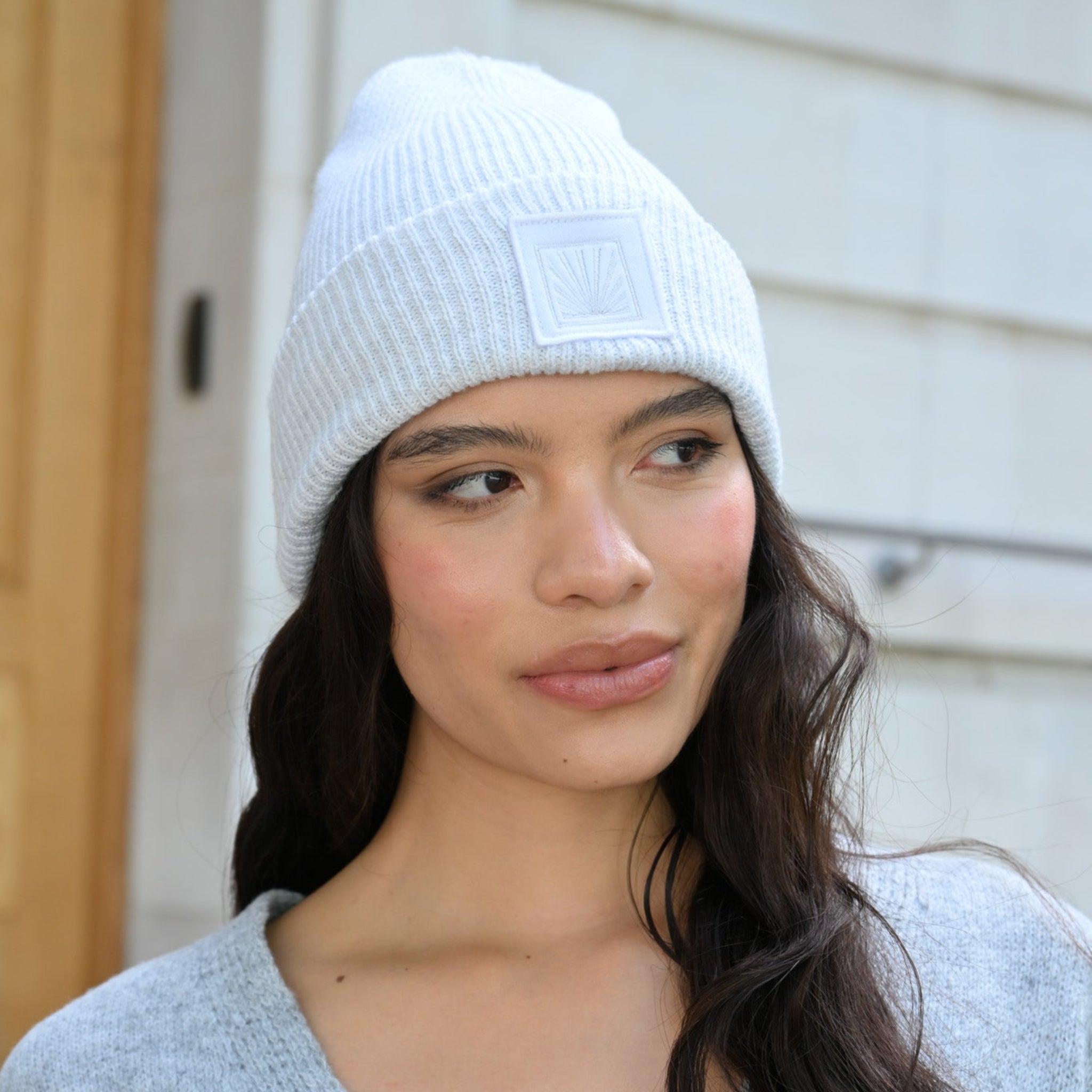Woman wearing a white knit beanie and gray cardigan outdoors.
