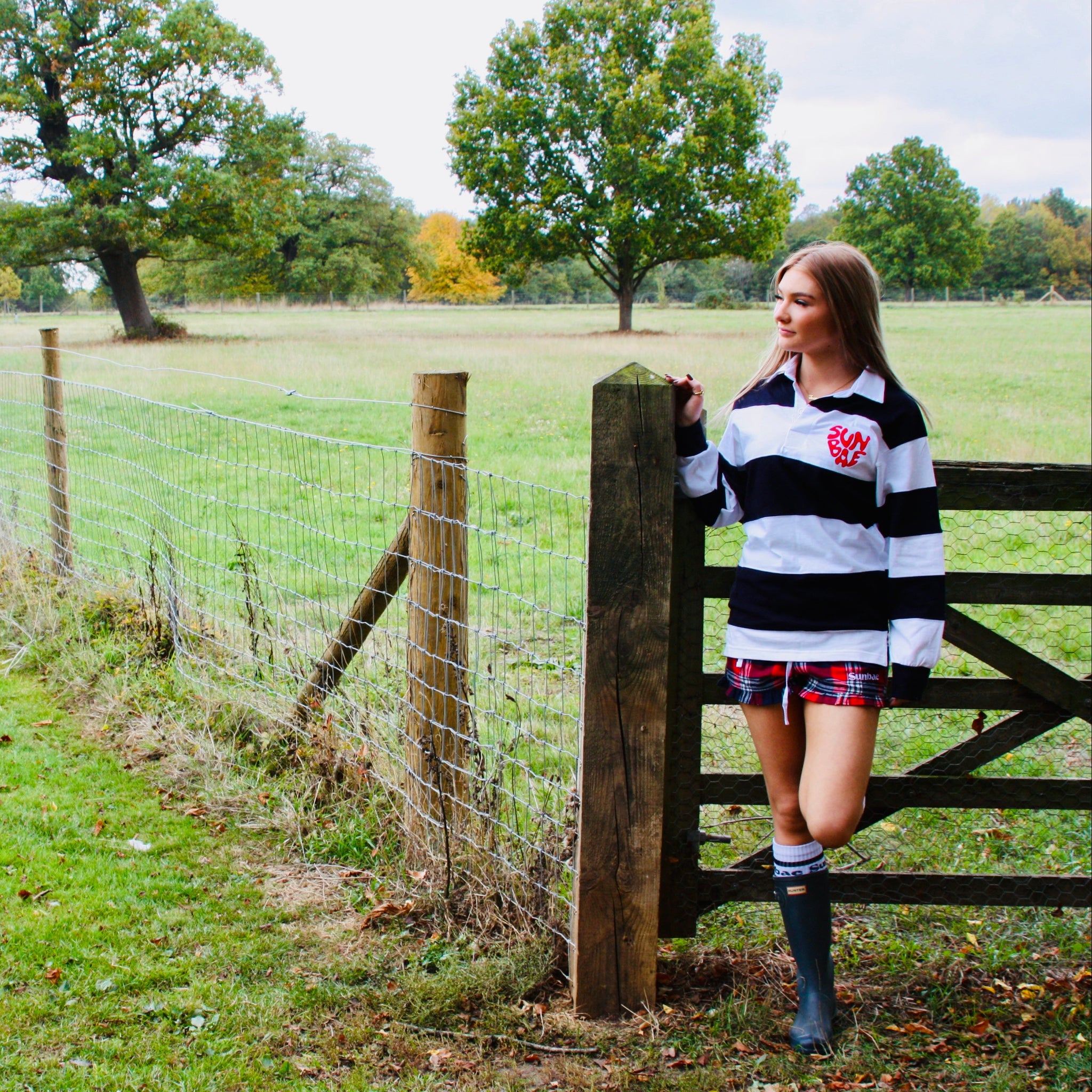 Woman in a rugby jersey standing by a wooden gate in a field