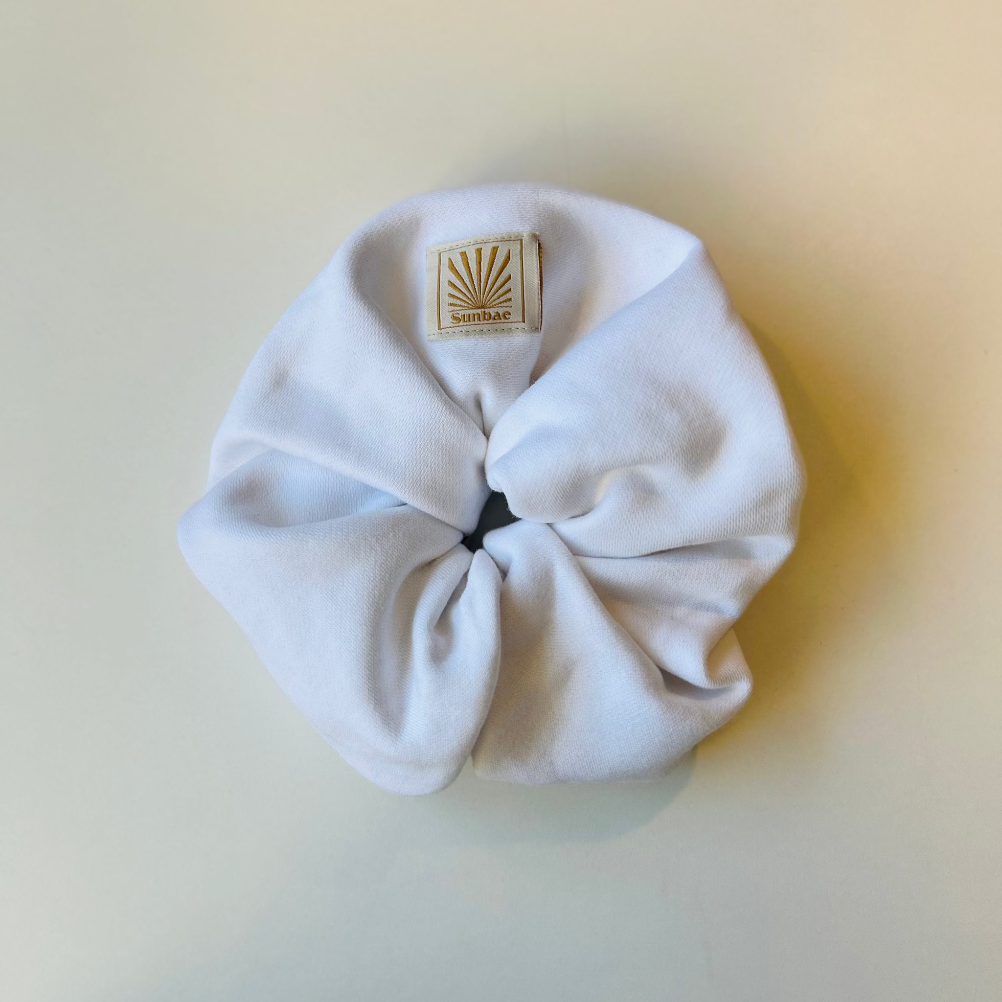 White SUNBAE scrunchie with a SUNBAE label on a light beige background.