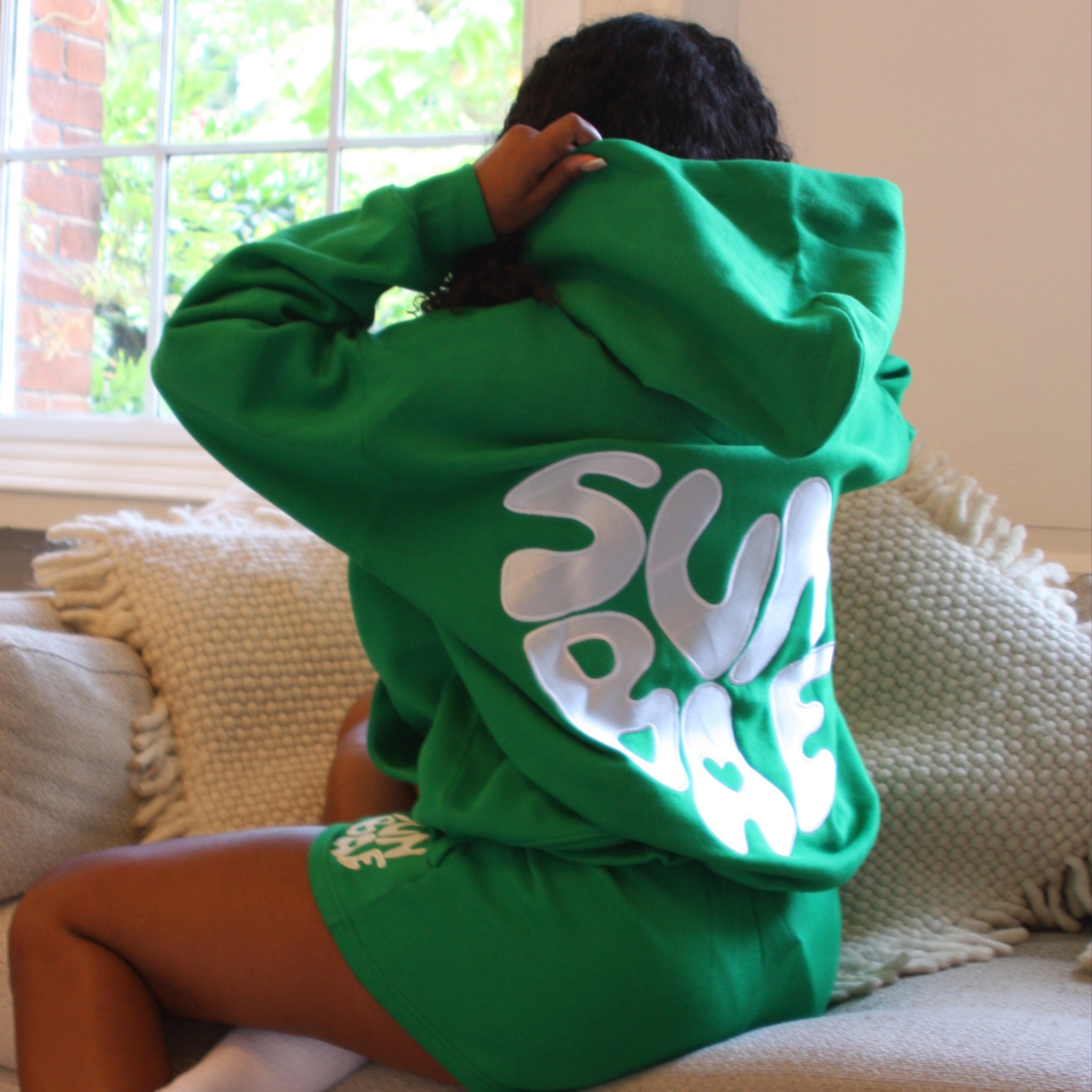 Sunbae Glower wearing SUNBAE Offline Oversize Hoodie with Glazed Heart Embroidery in Green sitting on a chair indoors.