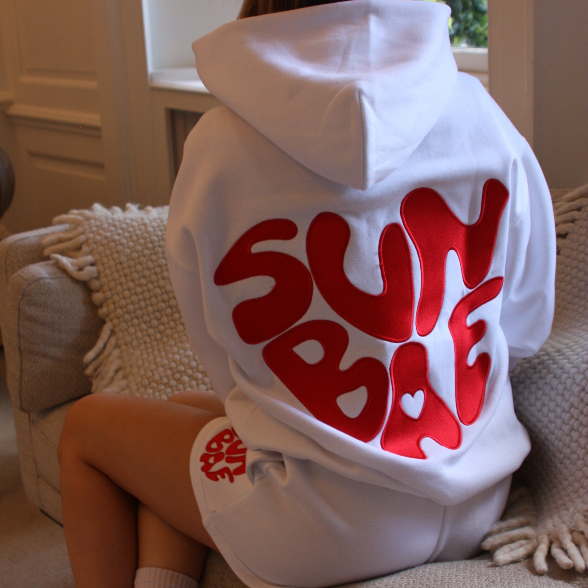 Sunbae Glower wearing Sunbae Offline Oversize Hoodie with Glazed Heart Embroidery in White sitting on a couch.