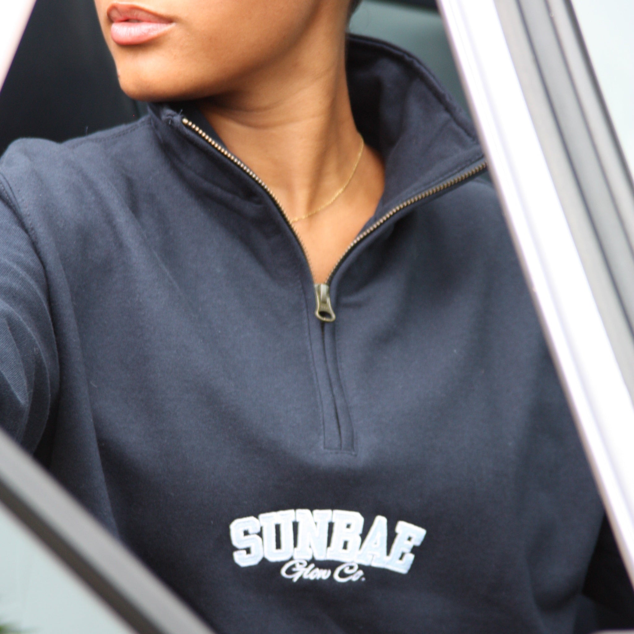 Person wearing a navy blue sweatshirt with 'SUNBAE' logo, sitting inside a vehicle.
