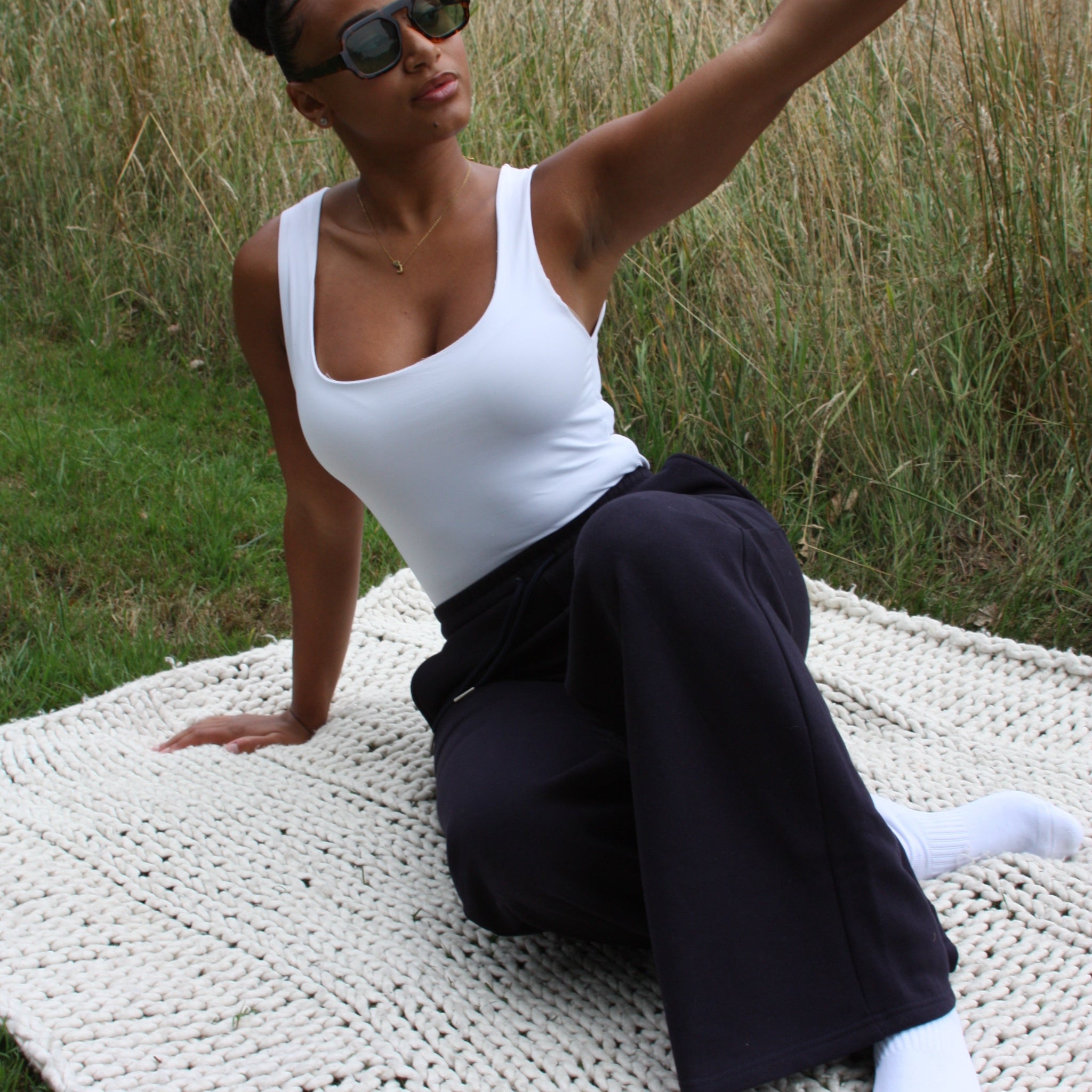 Woman sitting on a woven mat outdoors wearing Sunbae Sweat Pant with grass in the background