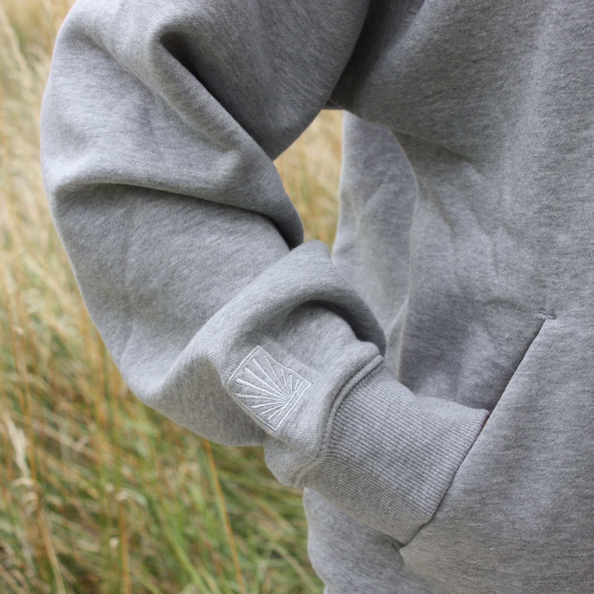 Grey Sunbae sweatshirt with a brand logo on the sleeve against a grassy background