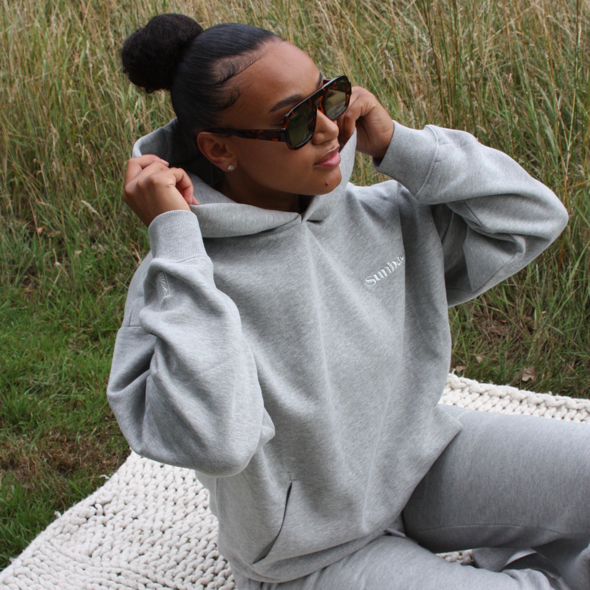 Person wearing a grey Sunbae hoodie with logo sitting in a grassy area.