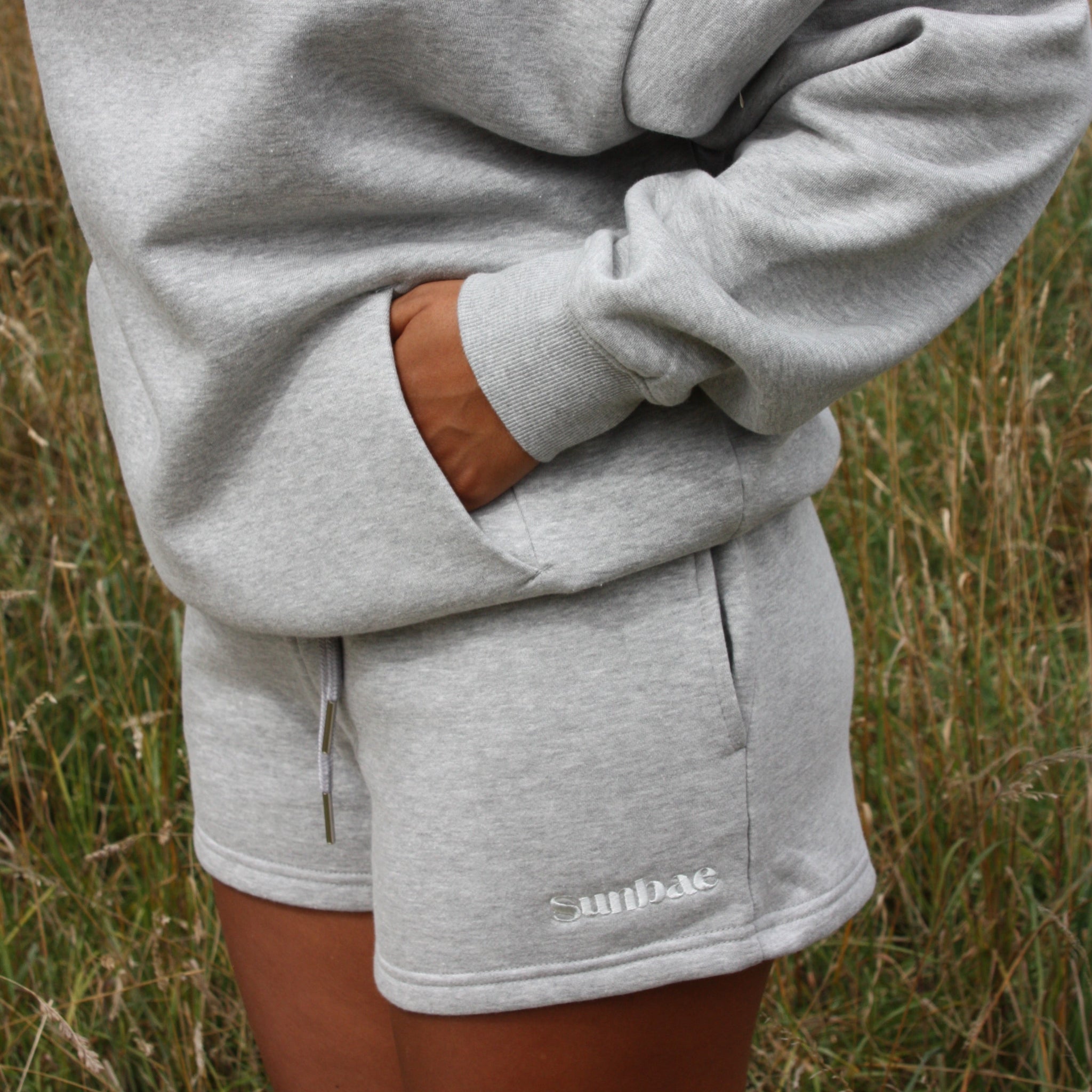 Person wearing a gray hoodie and shorts with 'Sunbae' branding in a grassy field.
