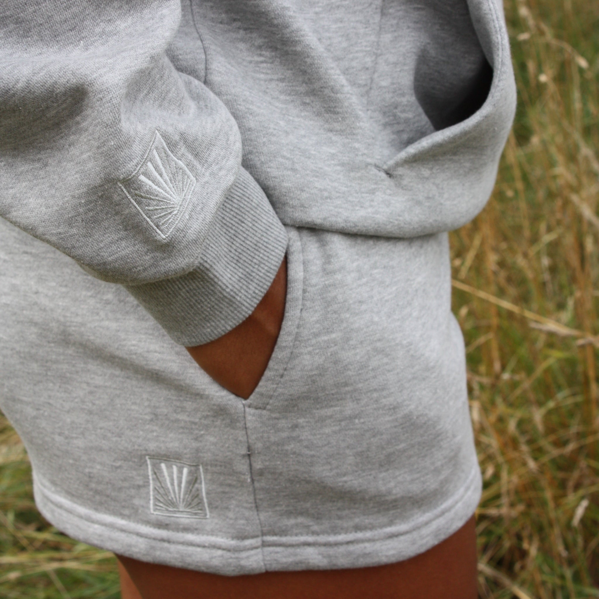 Gray Sunbae sweatshirt with a logo on a person standing in a grassy field