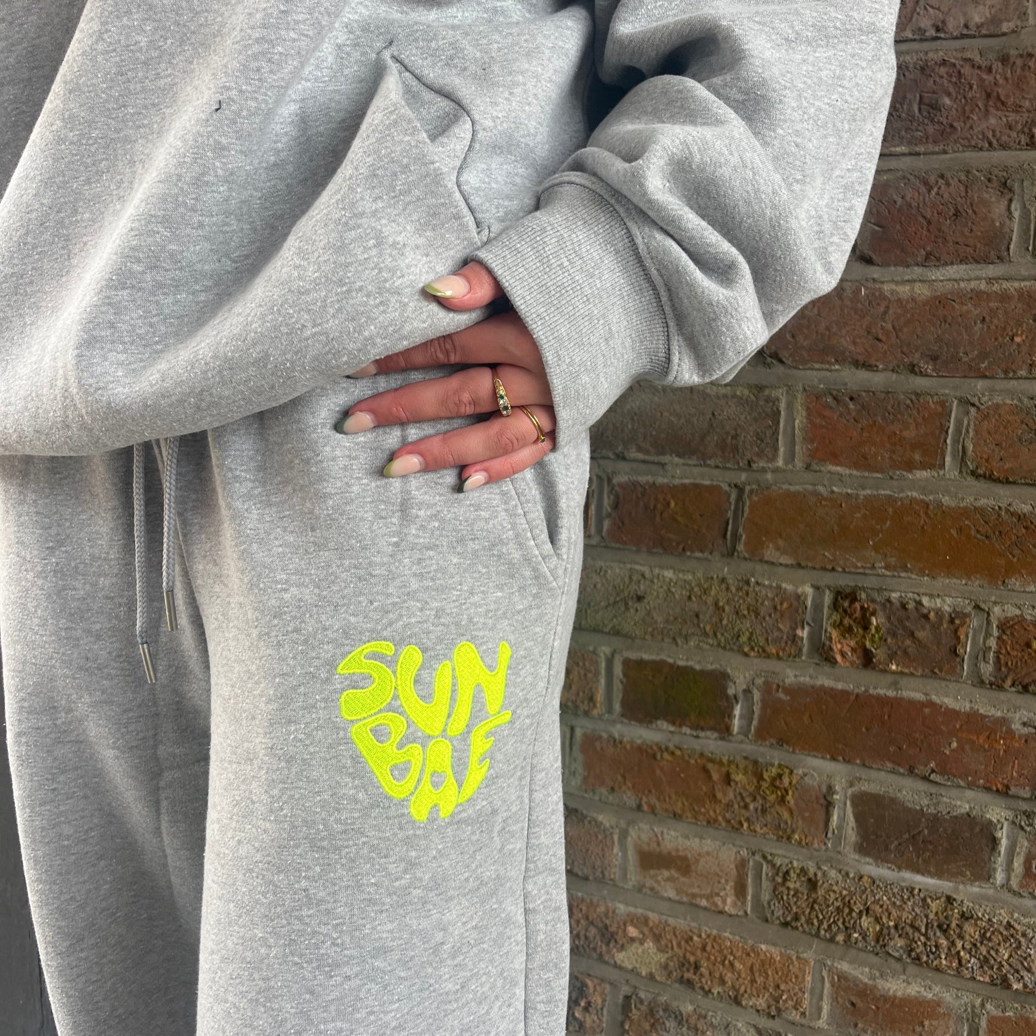 Grey SUNBAE sweatpants worn by a person against a brick wall.
