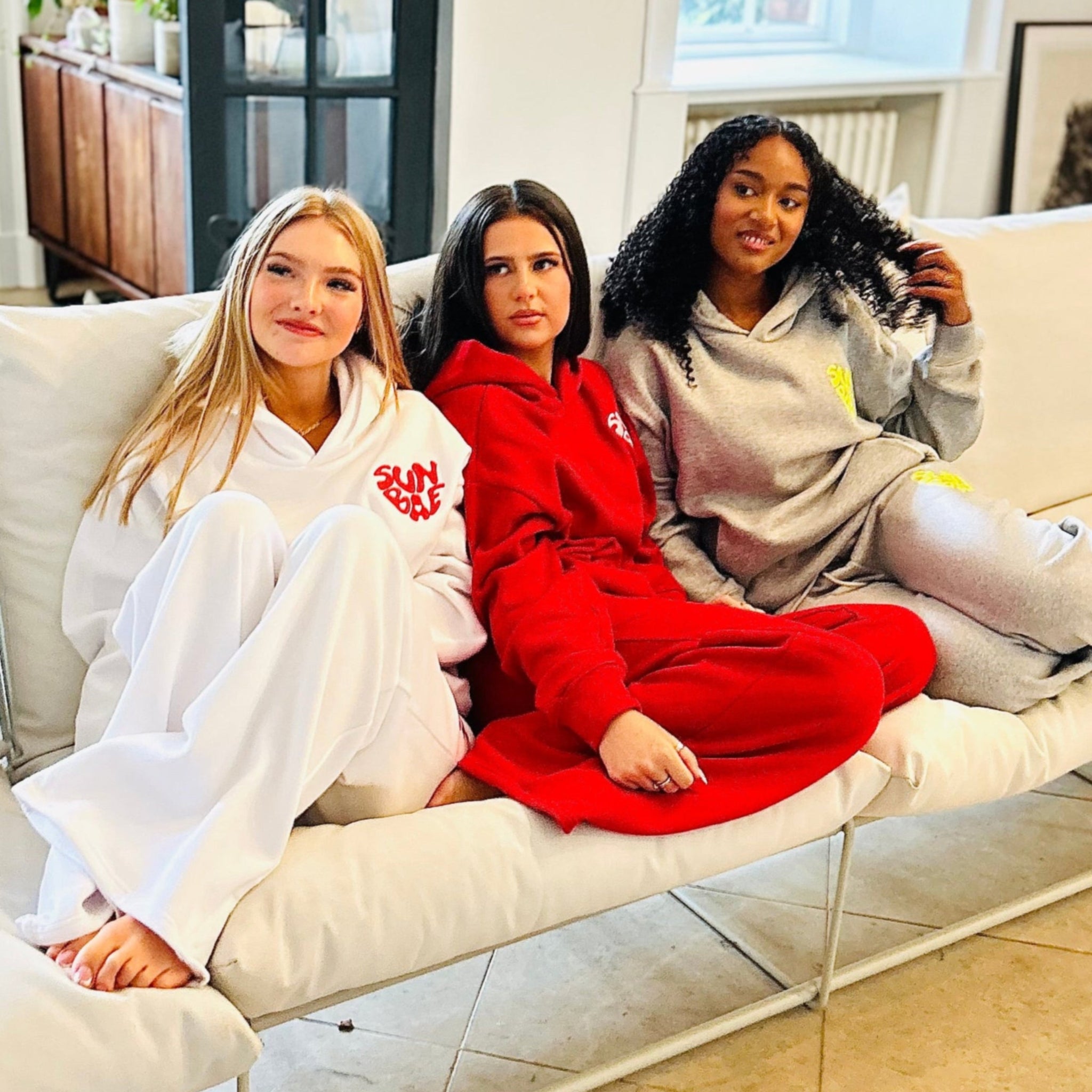 Sunbae Glow Collective sitting on a white couch wearing the Sunbae Glazed Heart Hoodie and the Sunbae Glazed Heart Sweat Pant