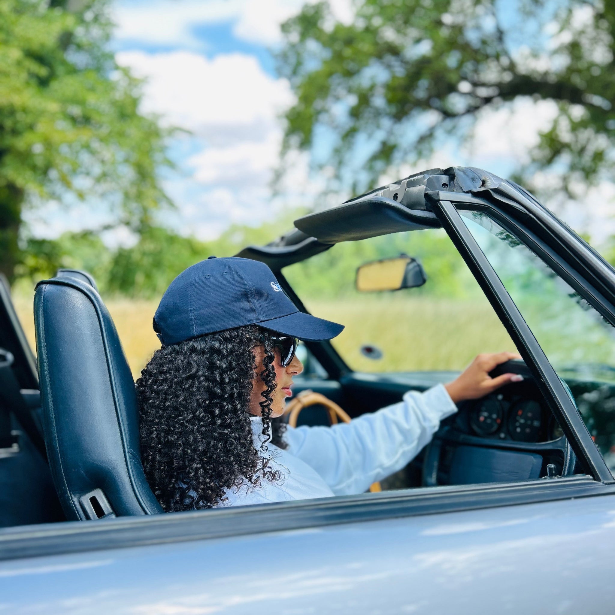 Person driving a convertible car with trees and blue sky in the background