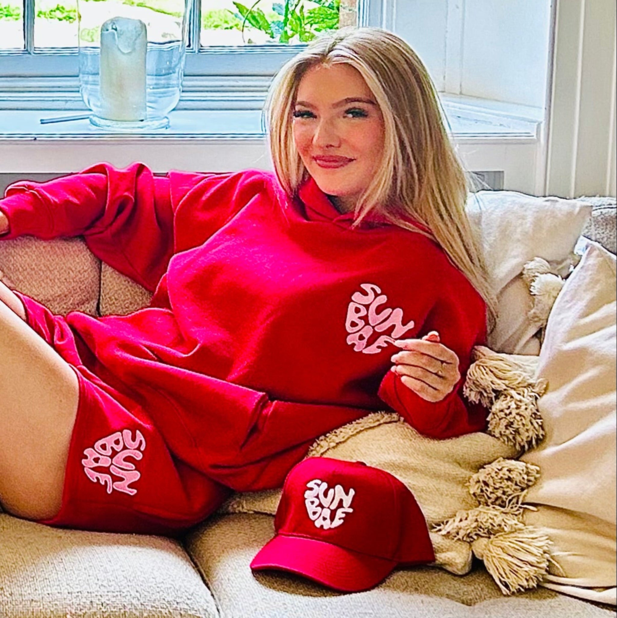 Woman in SUNBAE outift sitting on a couch in a bright room with large windows.