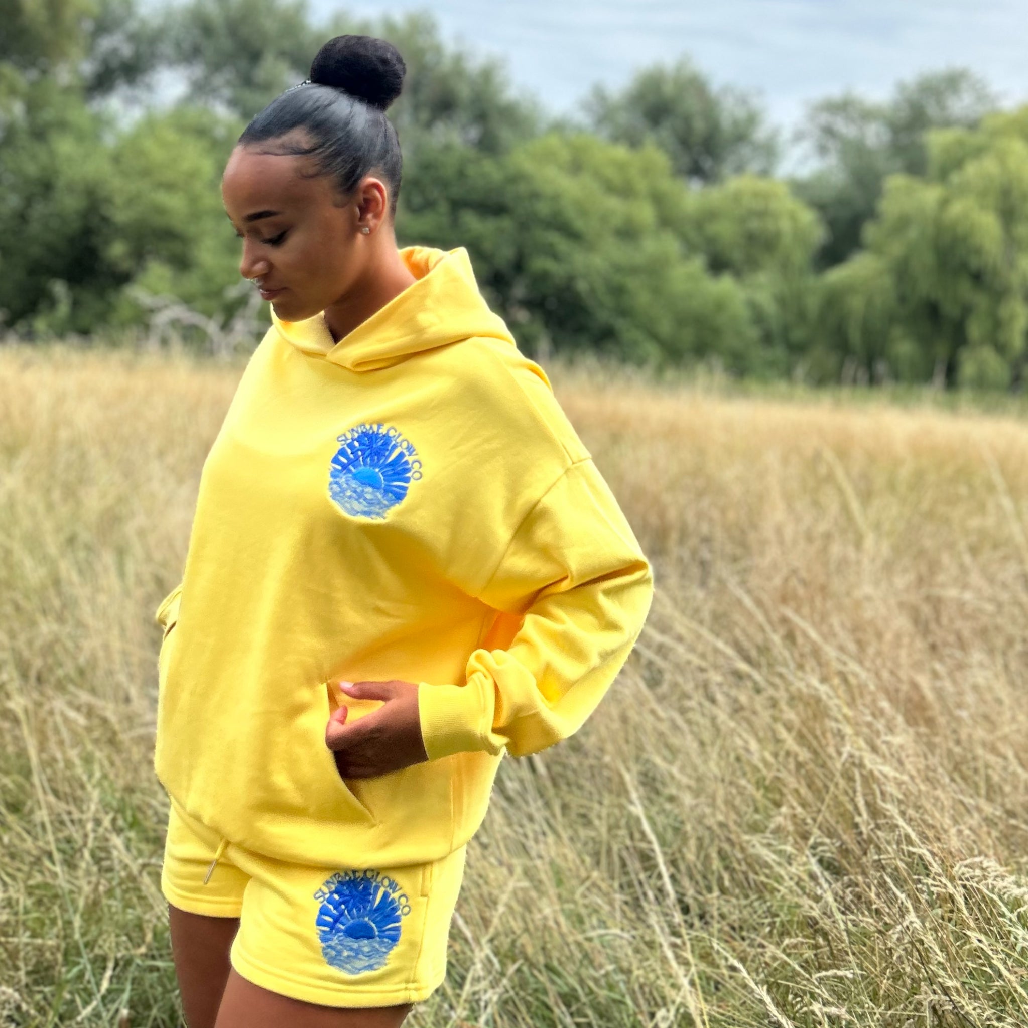 Person wearing a yellow Sunbae hoodie with blue circular designs in a field