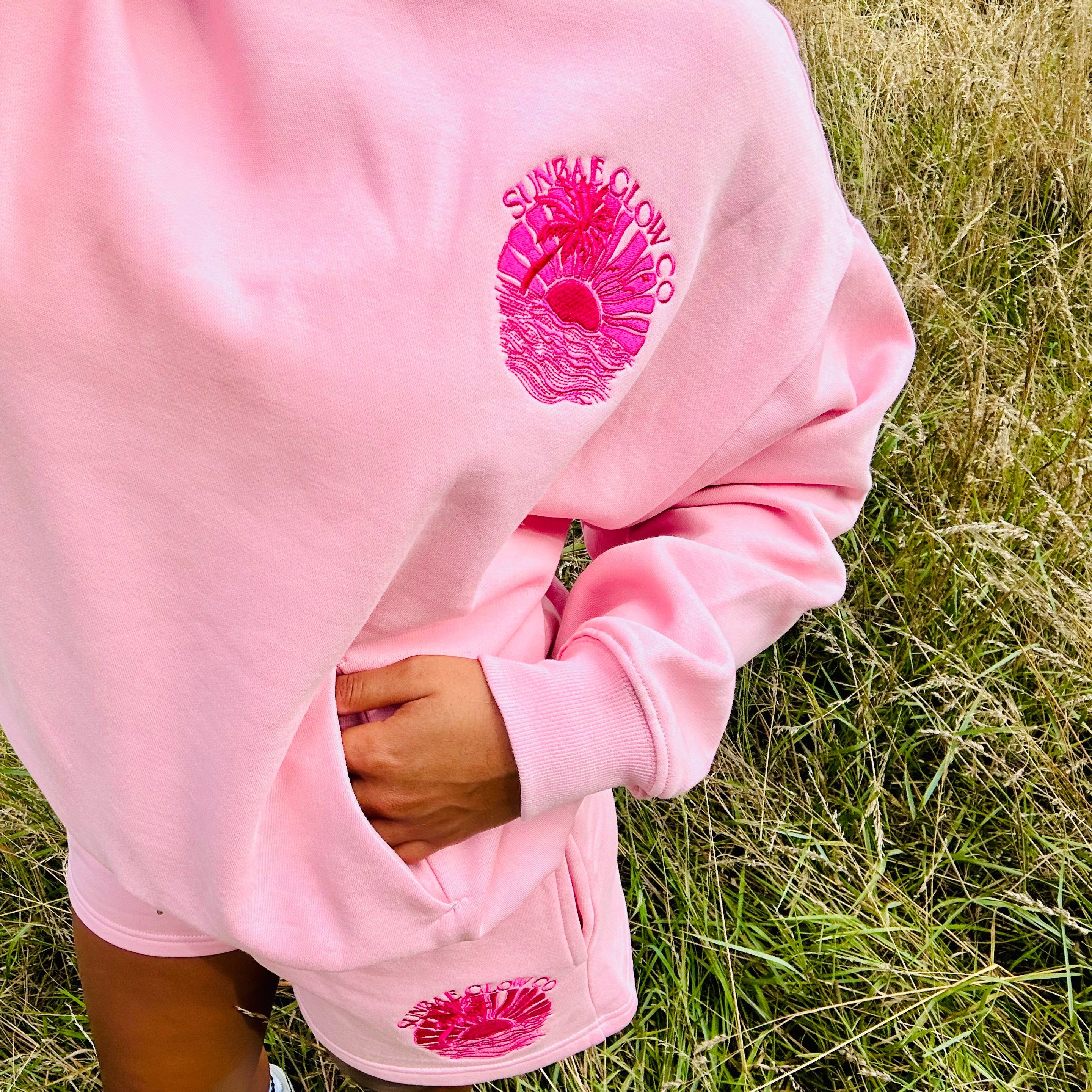 Person wearing a pink Sunbae hoodie with floral designs in a grassy field