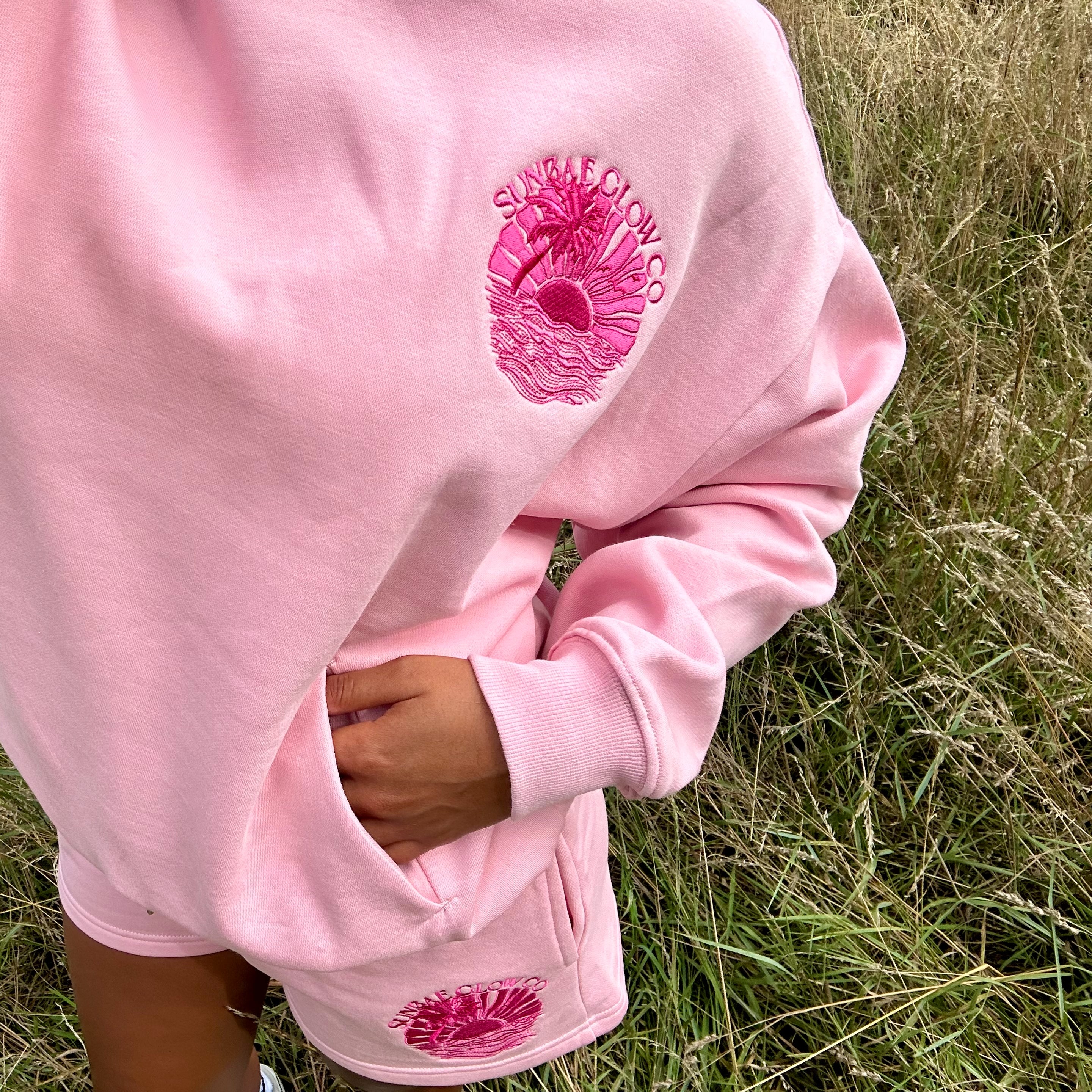 Person wearing a pink Sunbae hoodie with a logo in a grassy field