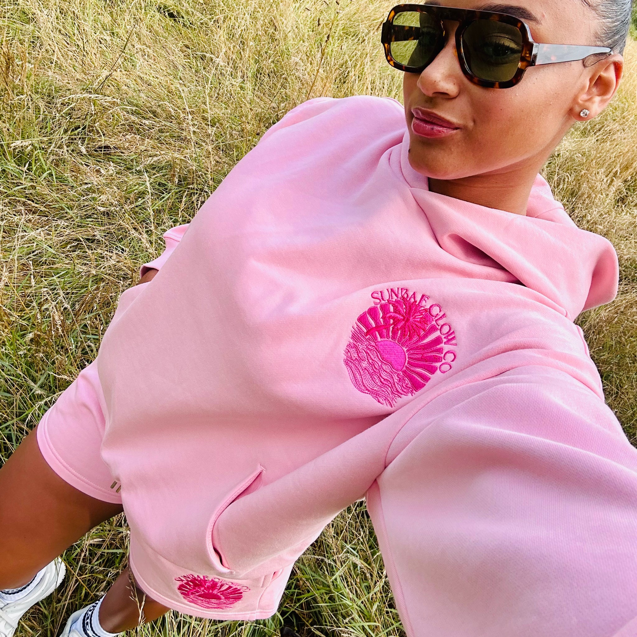 Person wearing a pink Sunbae hoodie with a logo in a grassy field