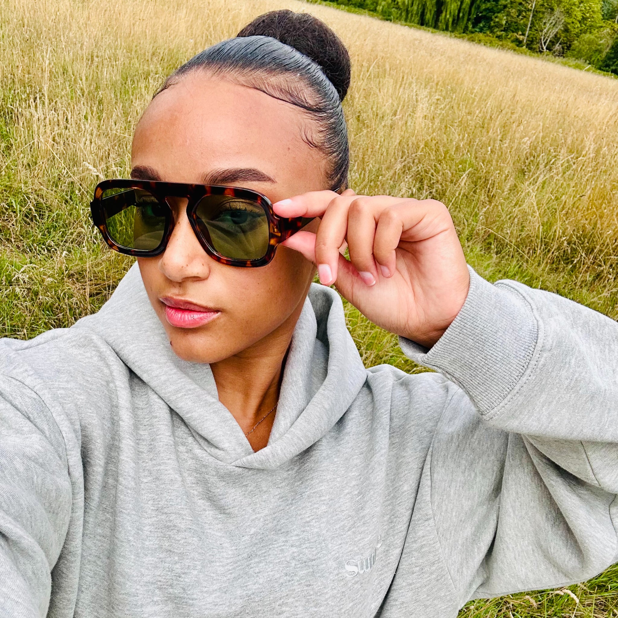 Woman wearing sunglasses and a grey Sunbae hoodie in a grassy field