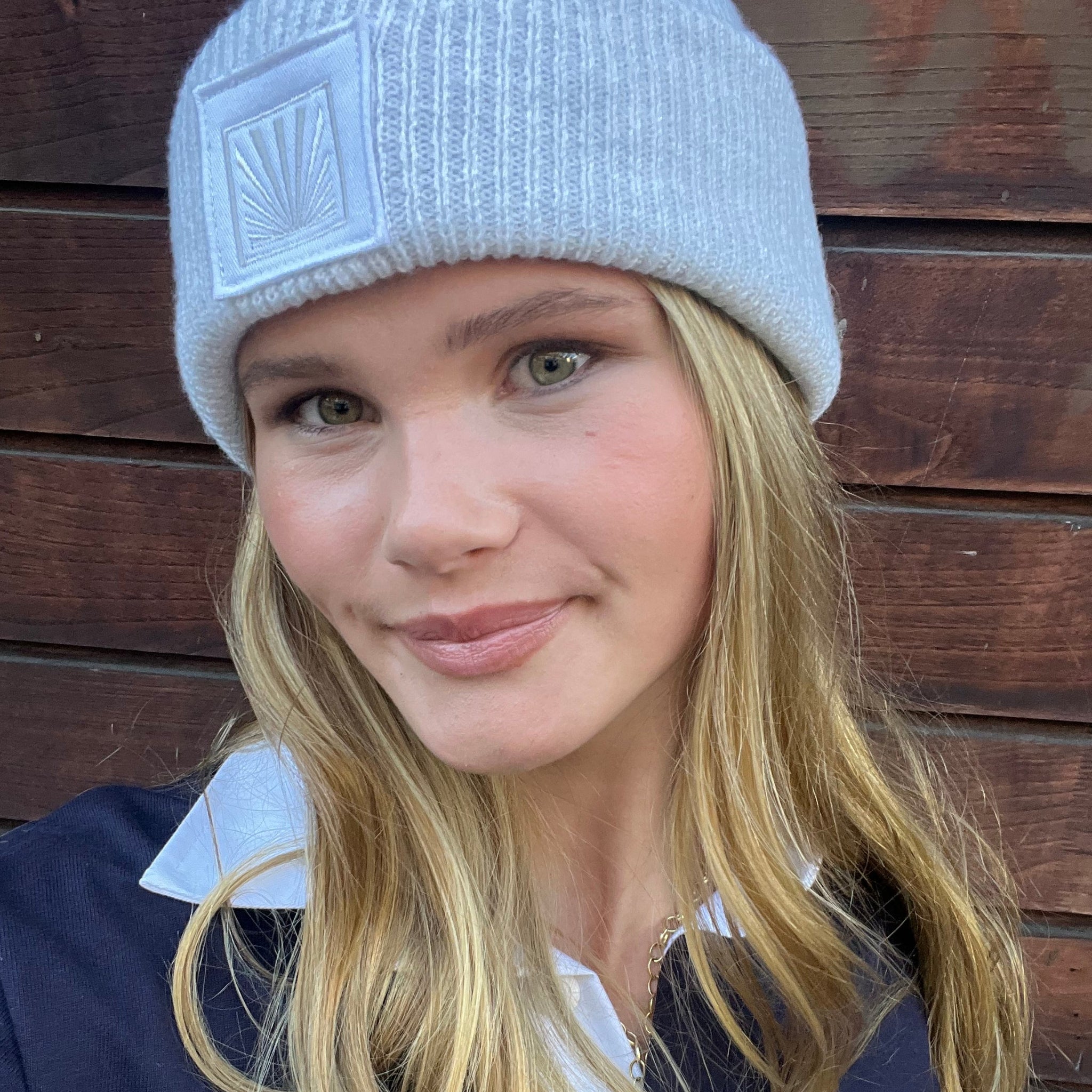 Person wearing a gray beanie with a logo against a wooden background