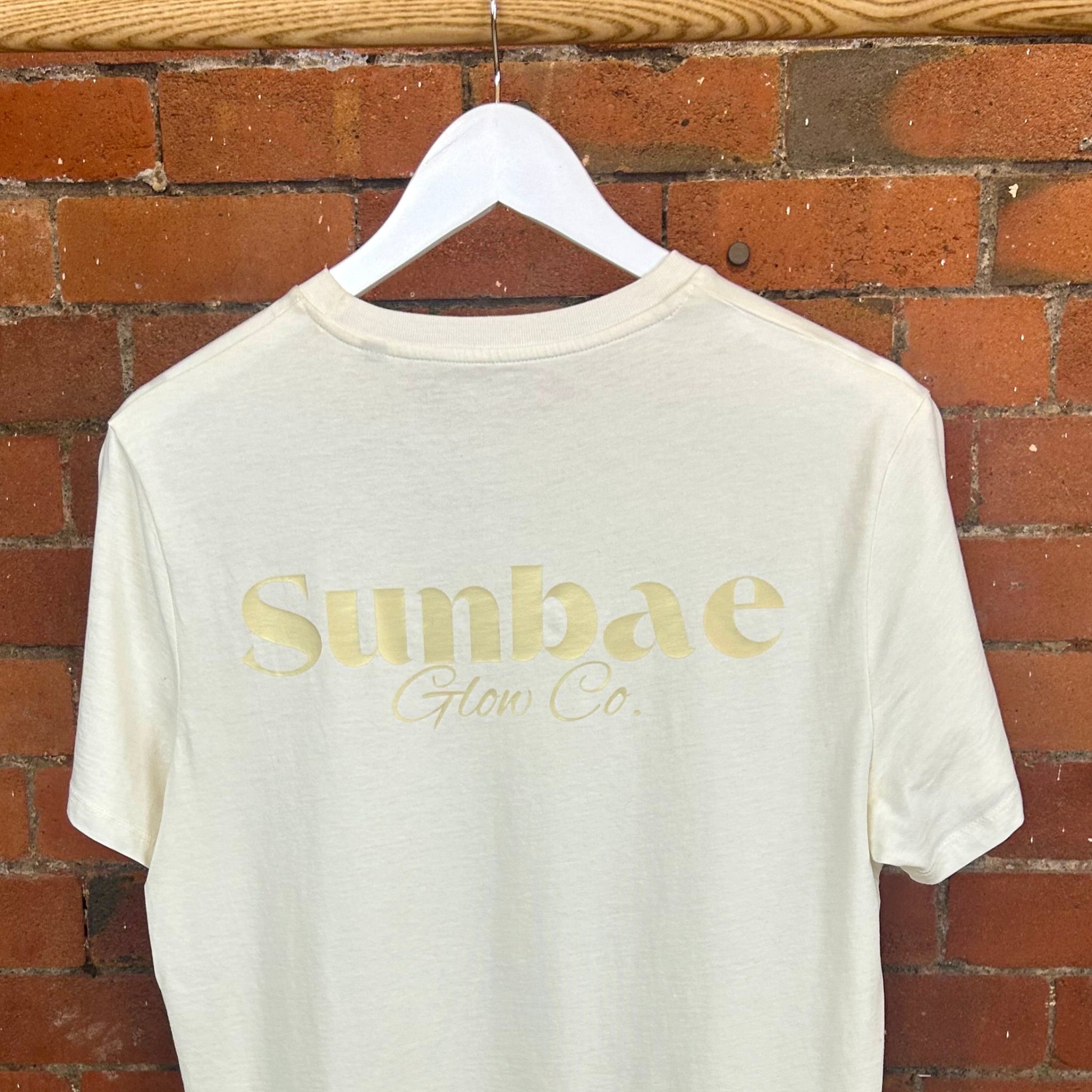 White t-shirt with 'Sunbae' logo on a hanger against a brick wall.