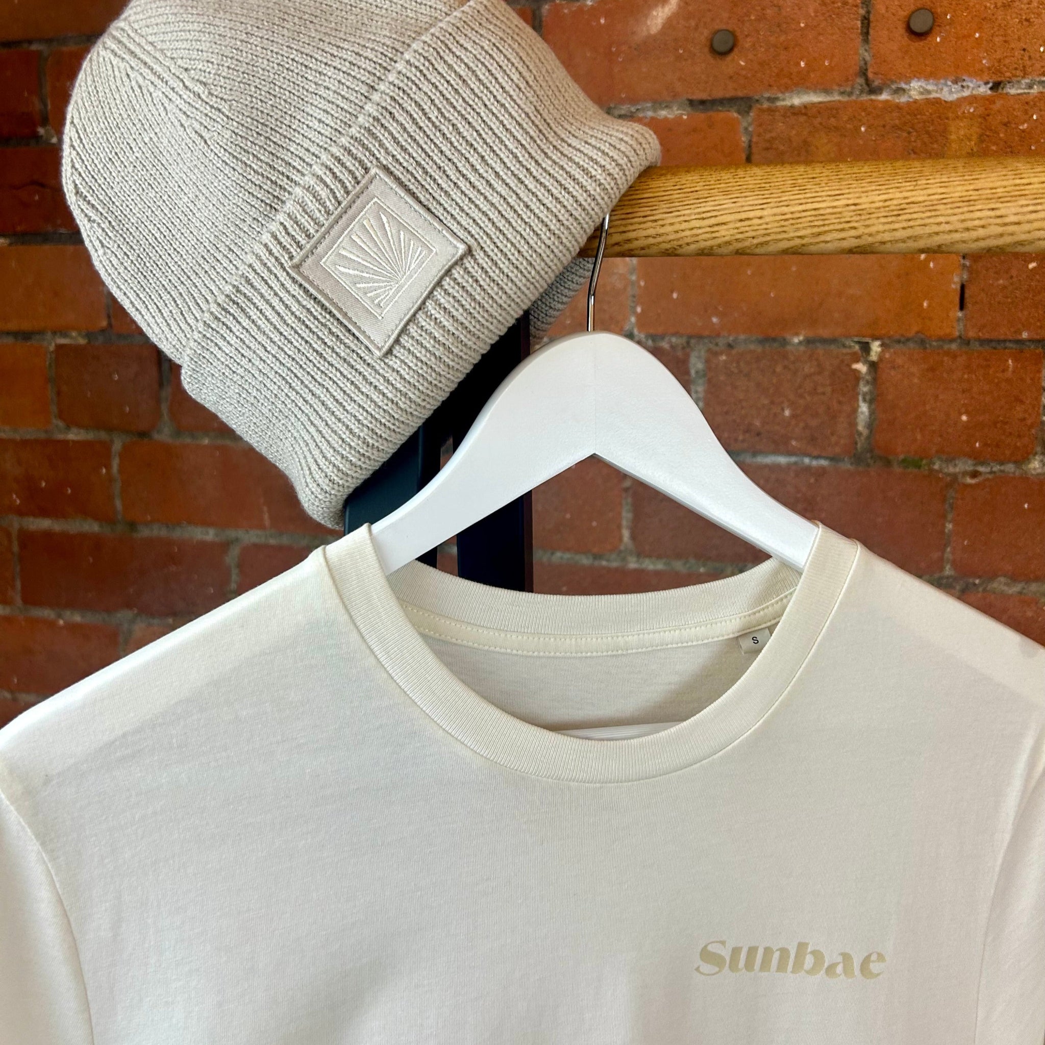 Beige beanie and sweatshirt with 'Sunbae' branding against a brick wall.