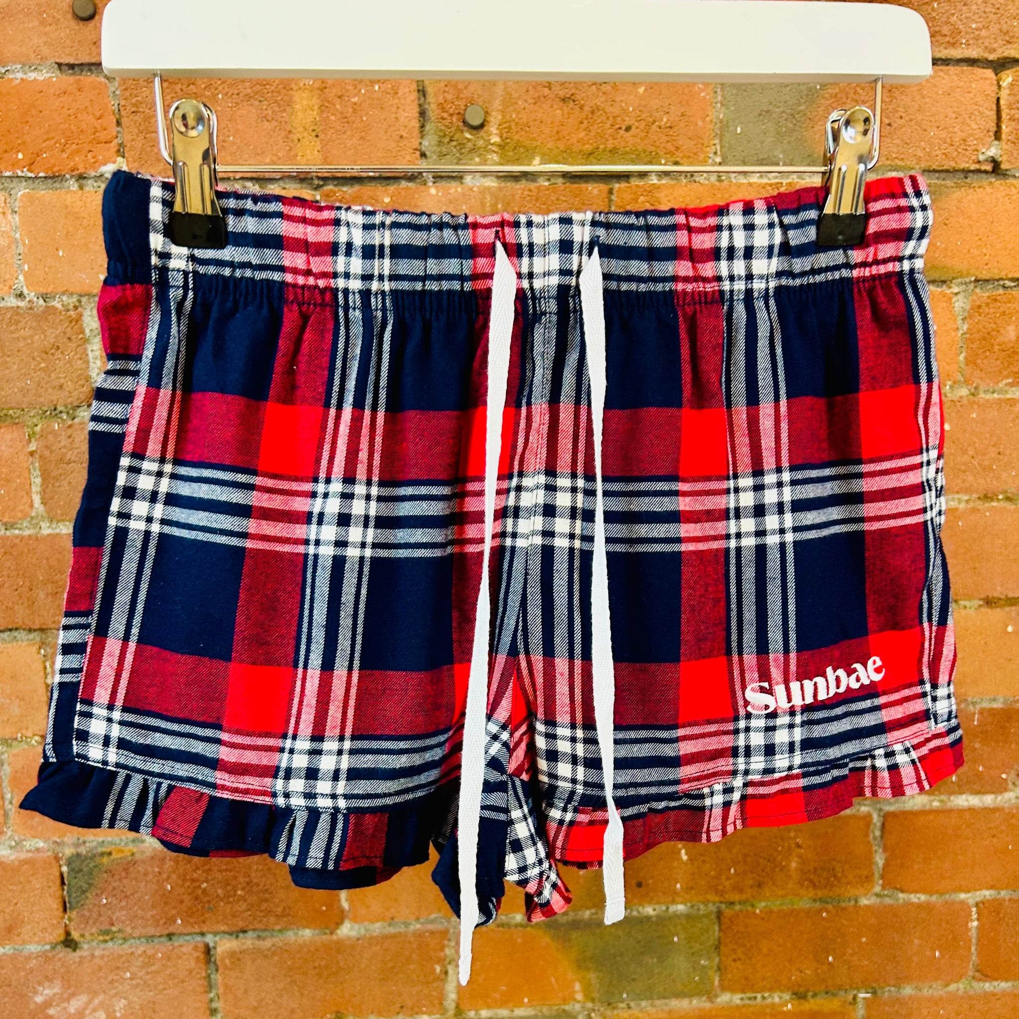 Plaid shorts with SUNBAE logo hanging on a brick wall.