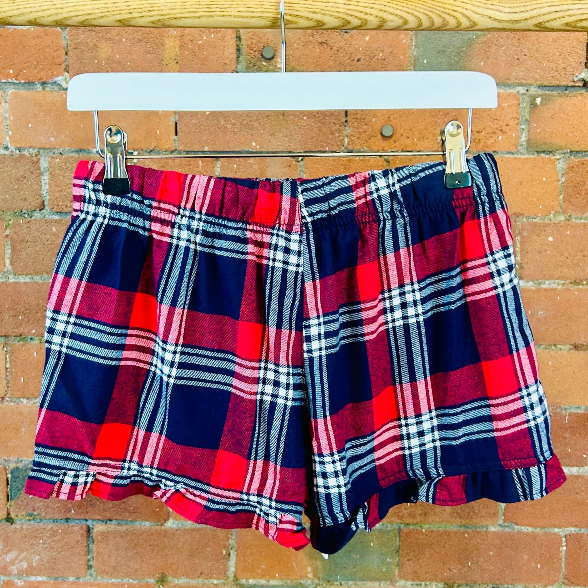 Plaid SUNBAE shorts hanging on a wooden rack against a brick wall.