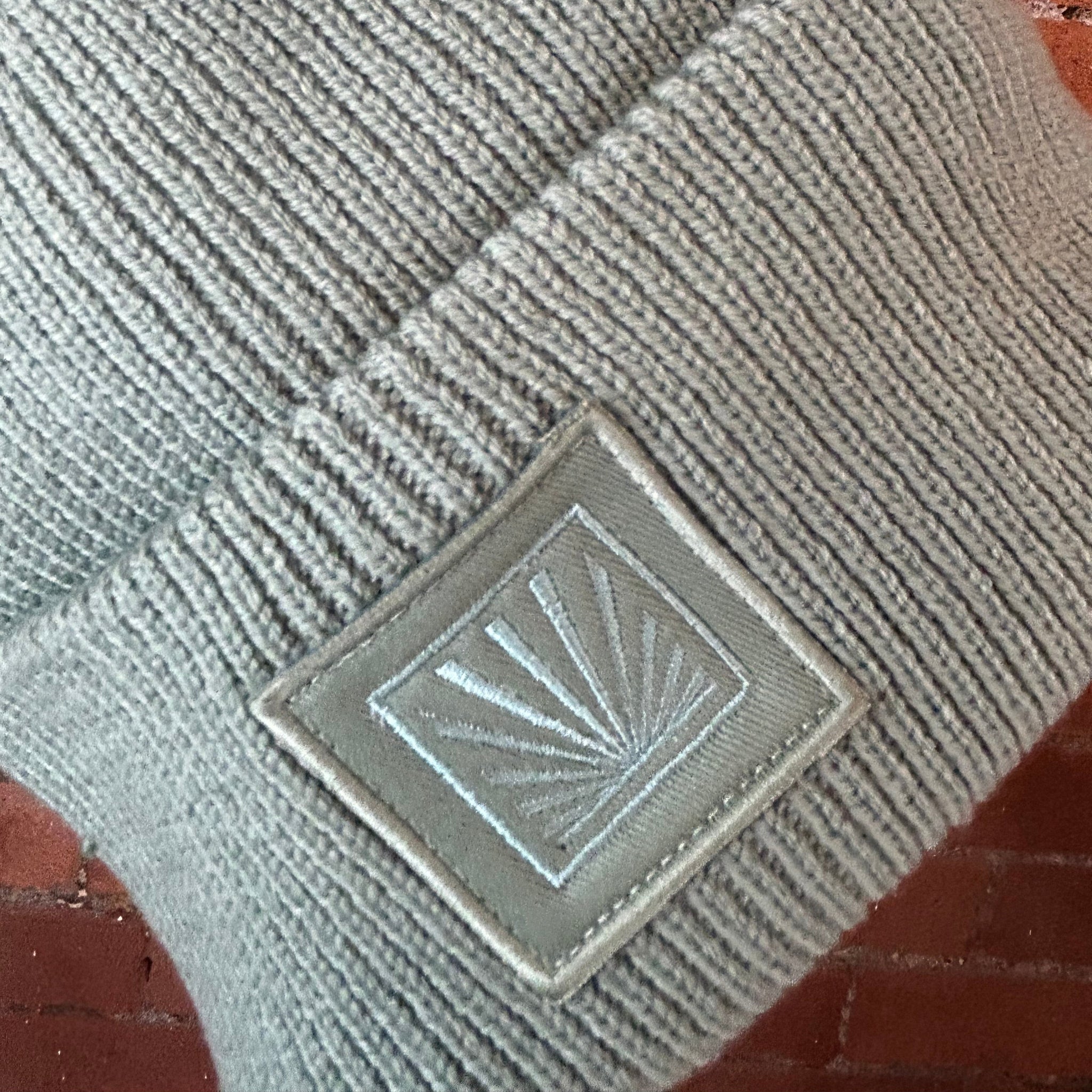 Gray textured fabric with a square patch featuring a sun design on a brick surface.
