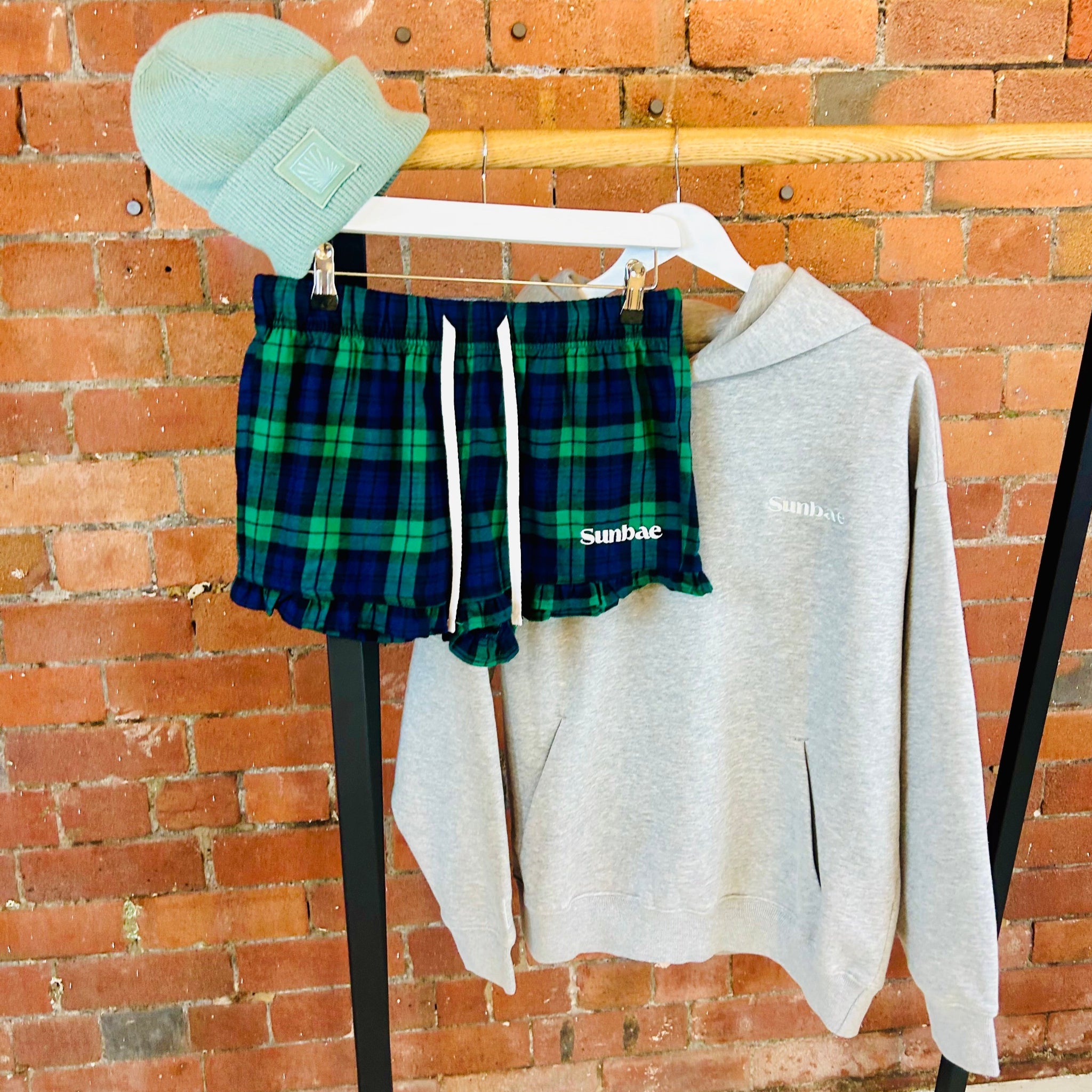 Plaid shorts and gray hoodie hanging on a rack against a brick wall.