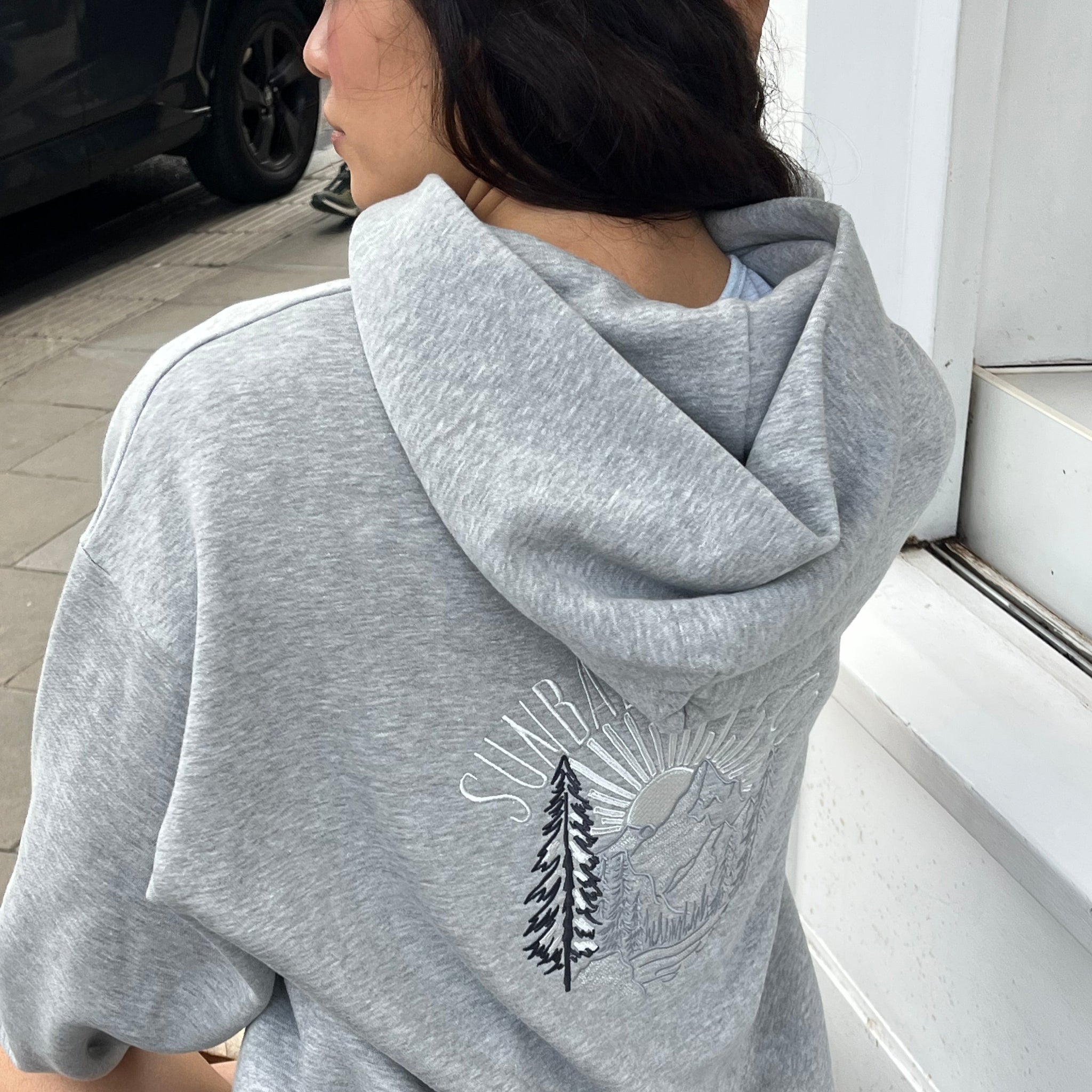 Person wearing a grey SUNBAE hoodie with a logo, standing indoors.