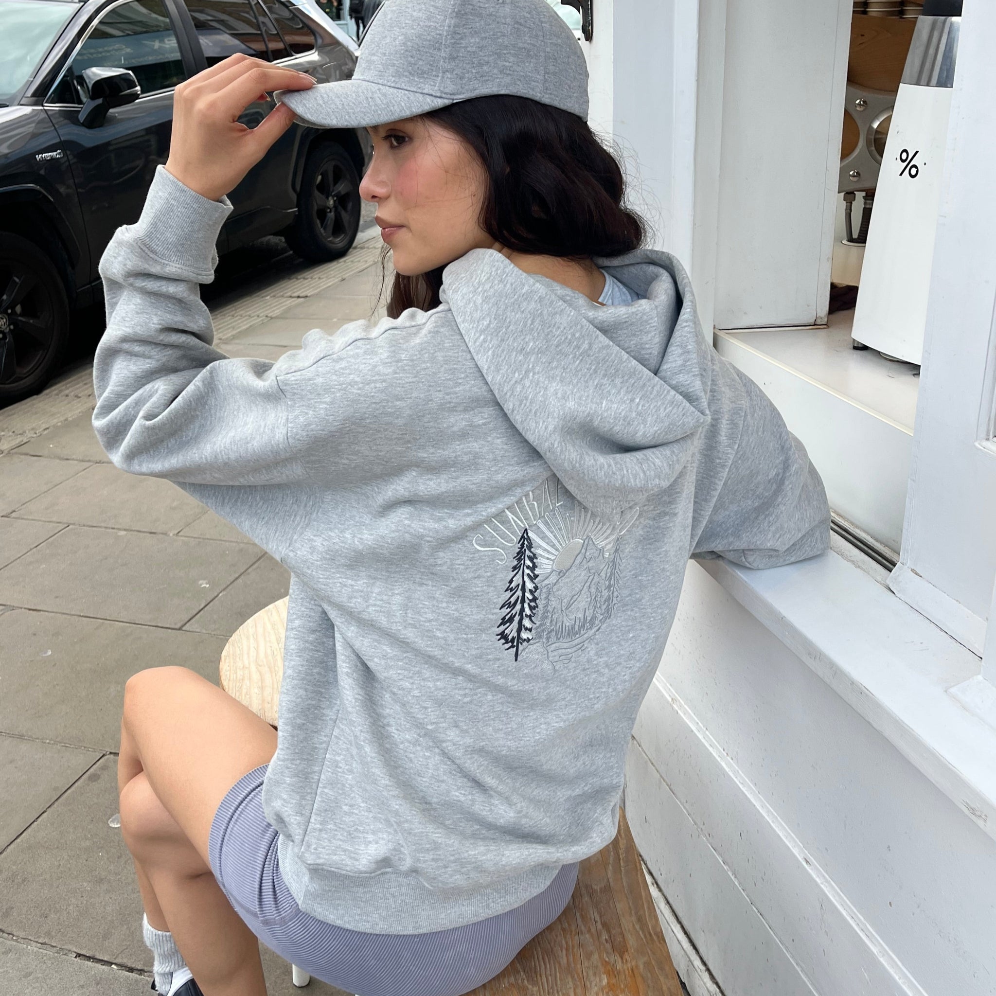 Person wearing a gray hoodie with a logo, standing next to a car.
