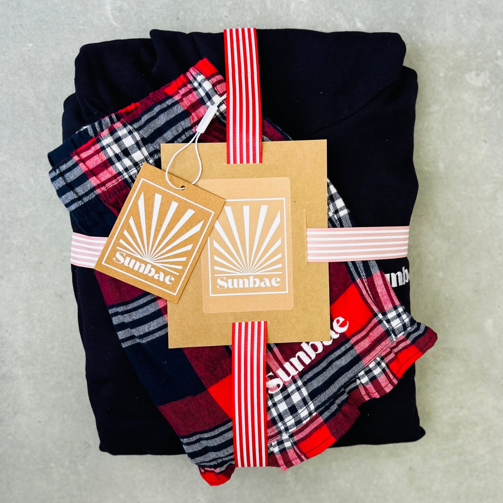 Folded black, red, and plaid fabric with Sunbac tags on a gray background