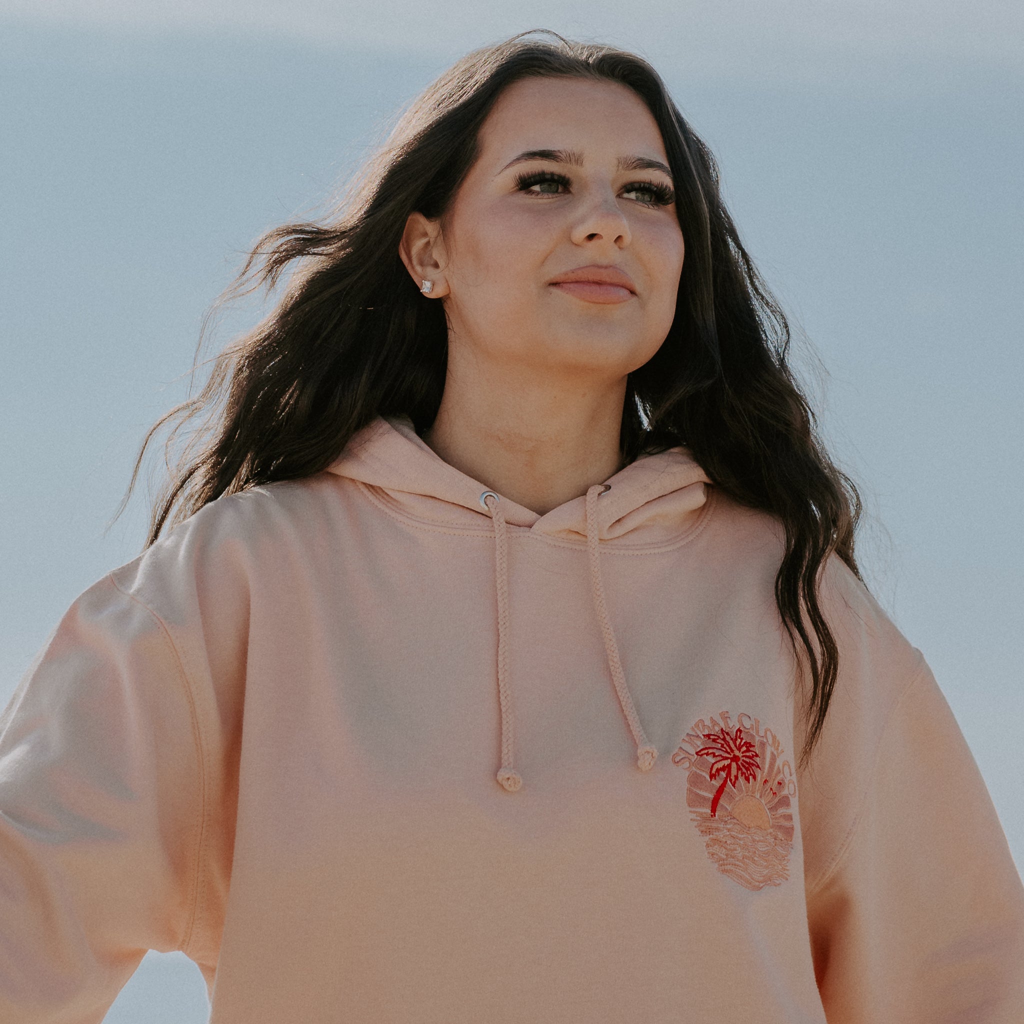 A woman wearing an oversized coral Sunbae hoodie with a graphic on the front.