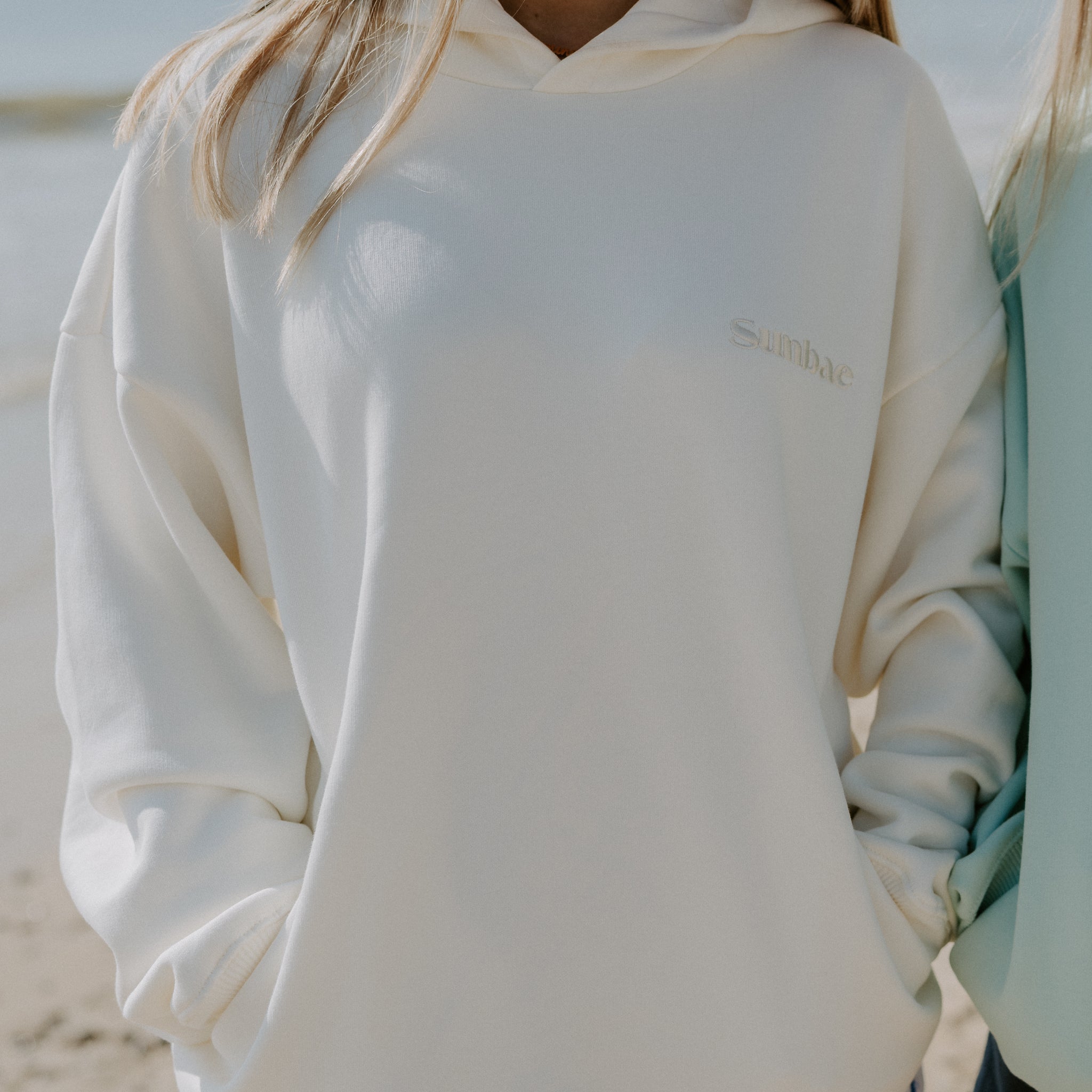 Person wearing ivory Sunbae hoodie on a beach.